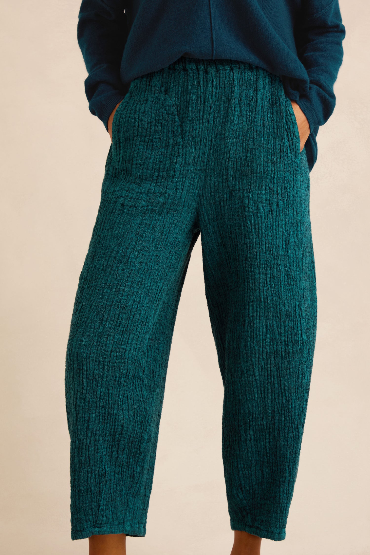 Model wearing Crinkle Linen Blend Bubble Trousers in teal, hands in pockets, shown from torso to feet against a plain background.