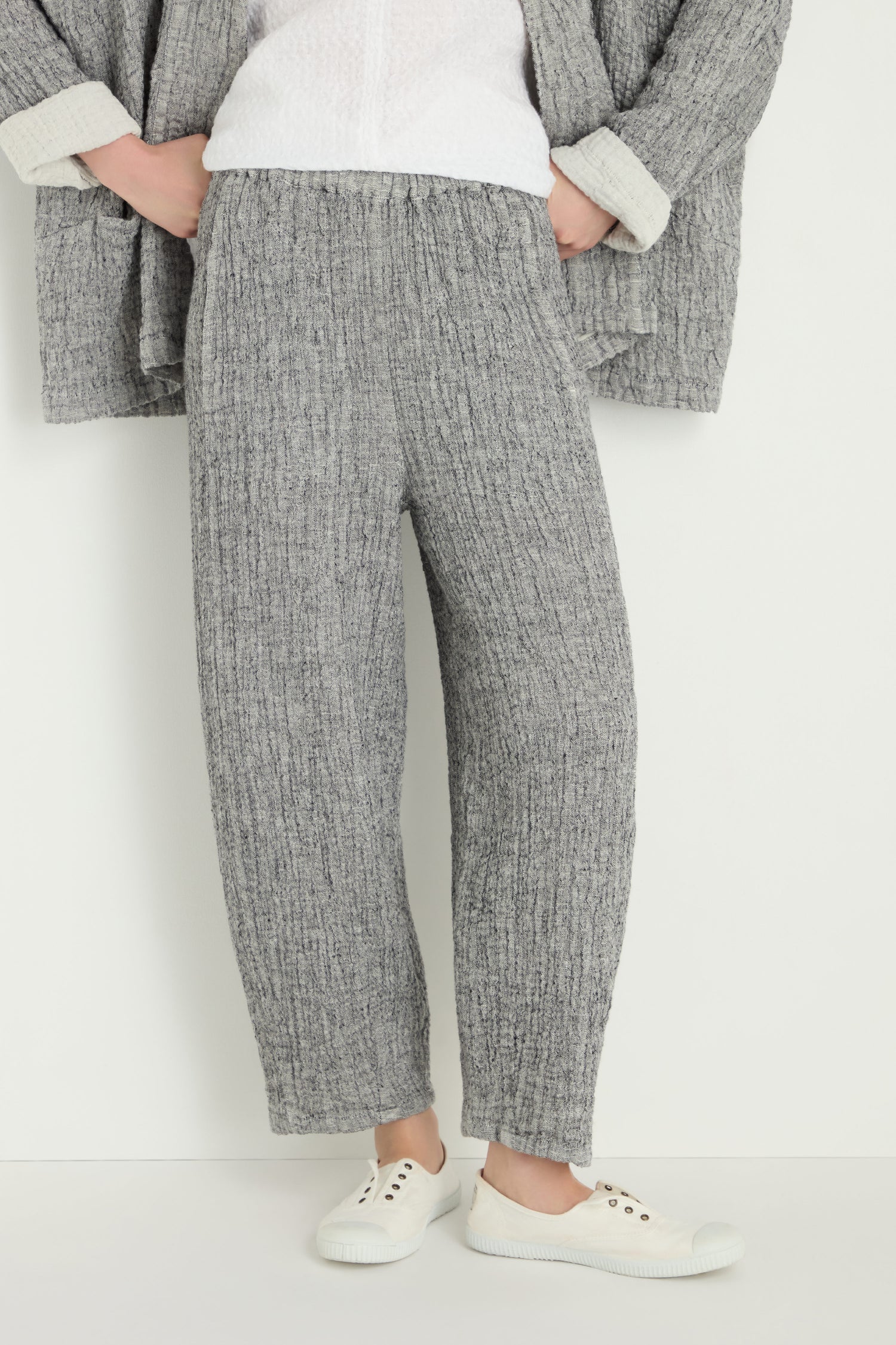 A person wears the Crinkle Double Face Linen Bubble Trouser in gray with a relaxed bubble fit, paired with a matching gray jacket, white top, and white sneakers, standing against a plain white background.