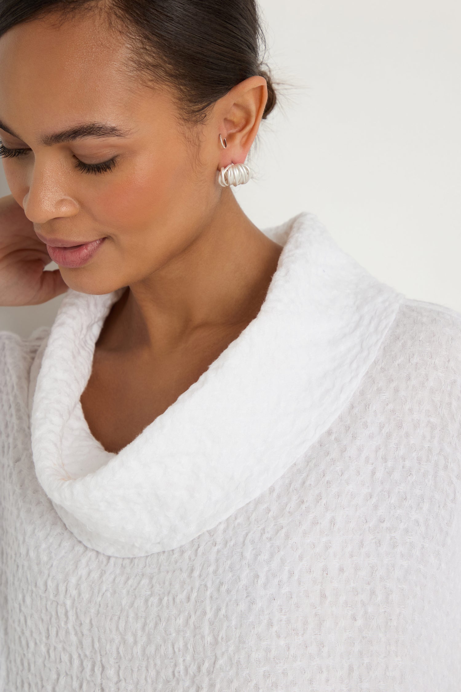 A woman, shown from the shoulders up against a plain background, wears the Waffle Linen Boxy Cowl Neck Top and silver hoop earrings.