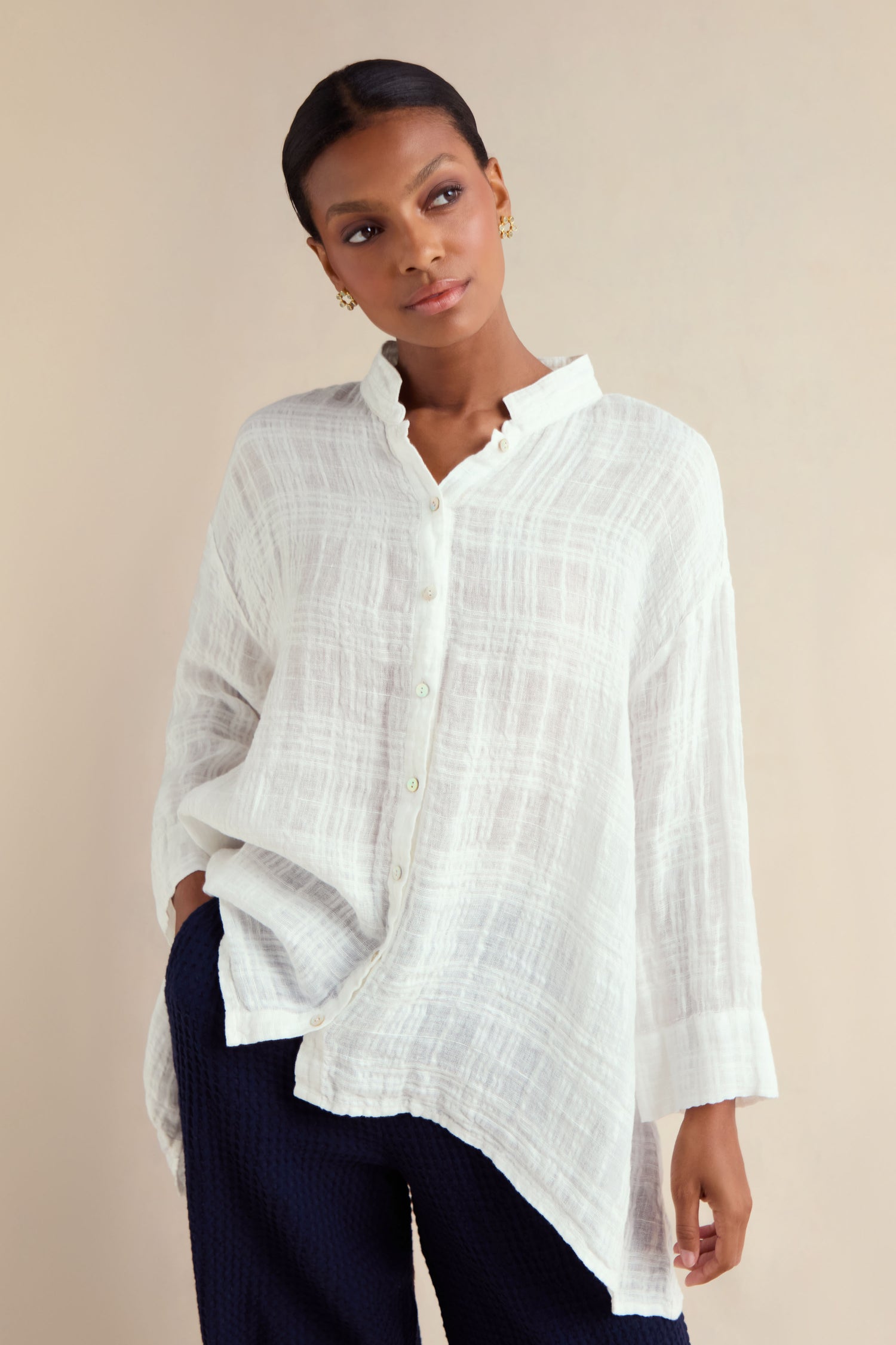 A woman models the Gauzy Linen Relaxed Shirt—an oversized white top—paired with dark pants, standing against a plain light background and looking slightly to the side.