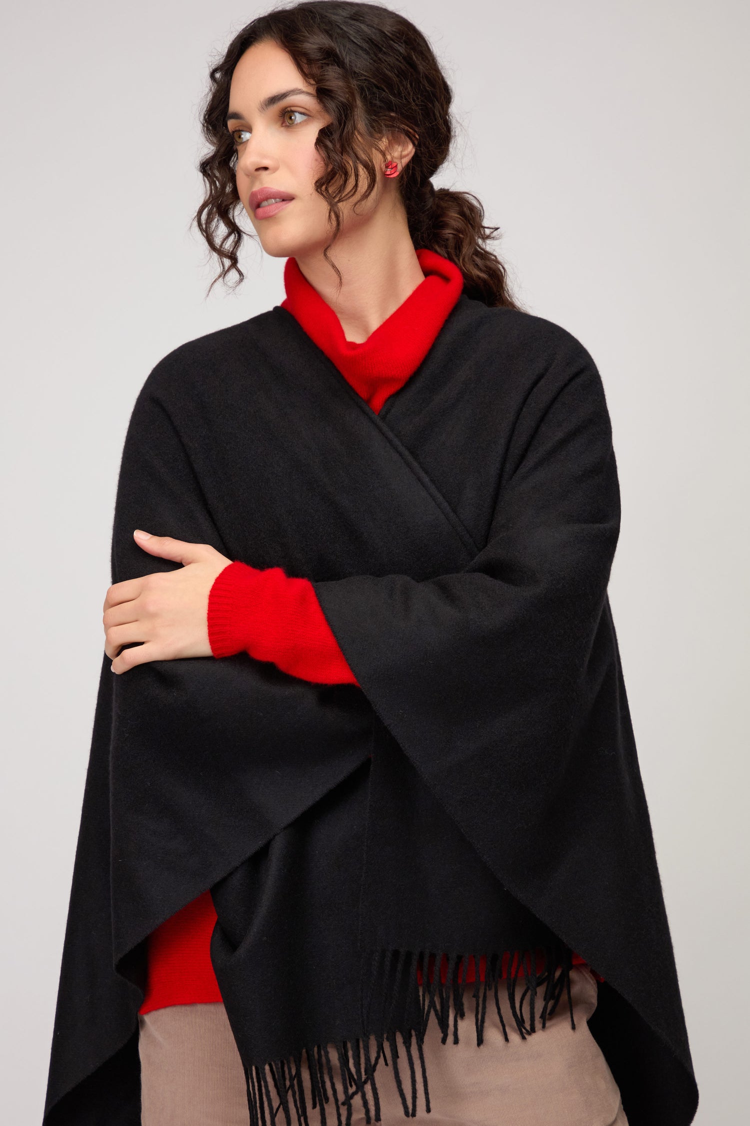 A woman with curly hair models the Wool Cashmere Black Shawl, draped over a red sweater and beige pants, standing against a plain light background.