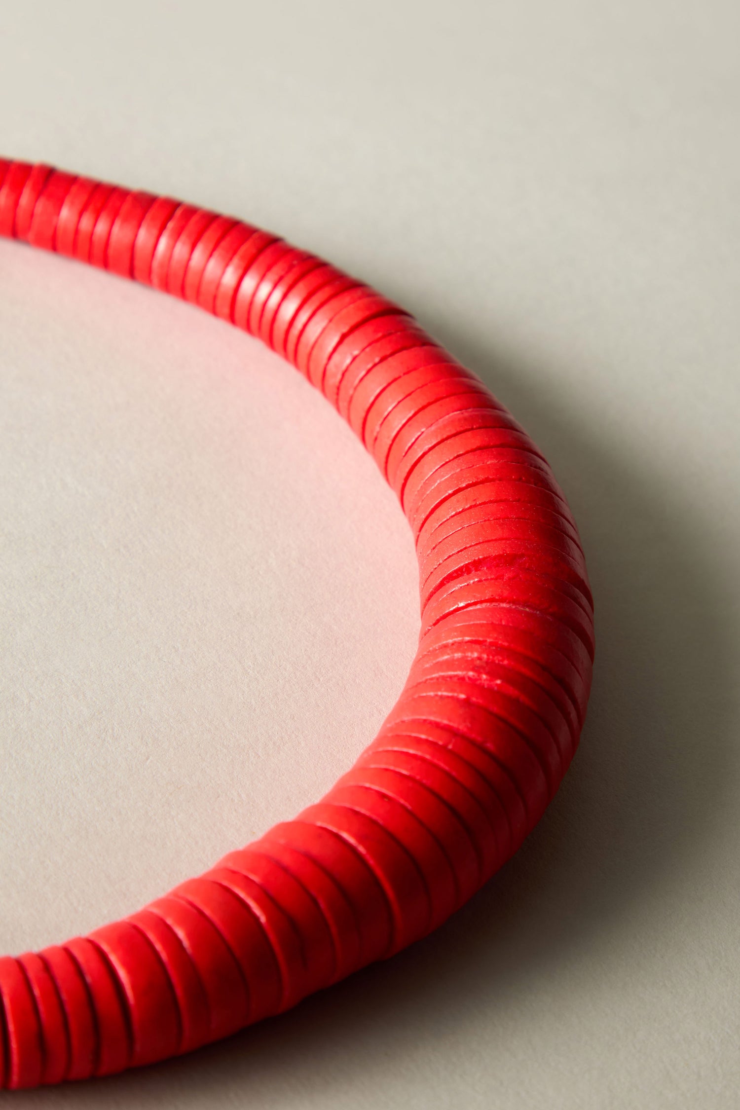 Close-up of a red, coiled object resembling a ribbed necklace against a neutral background. Its intricate design showcases the artistry behind the Graduated Coco Disc Necklace, hinting at Philippines craftsmanship.