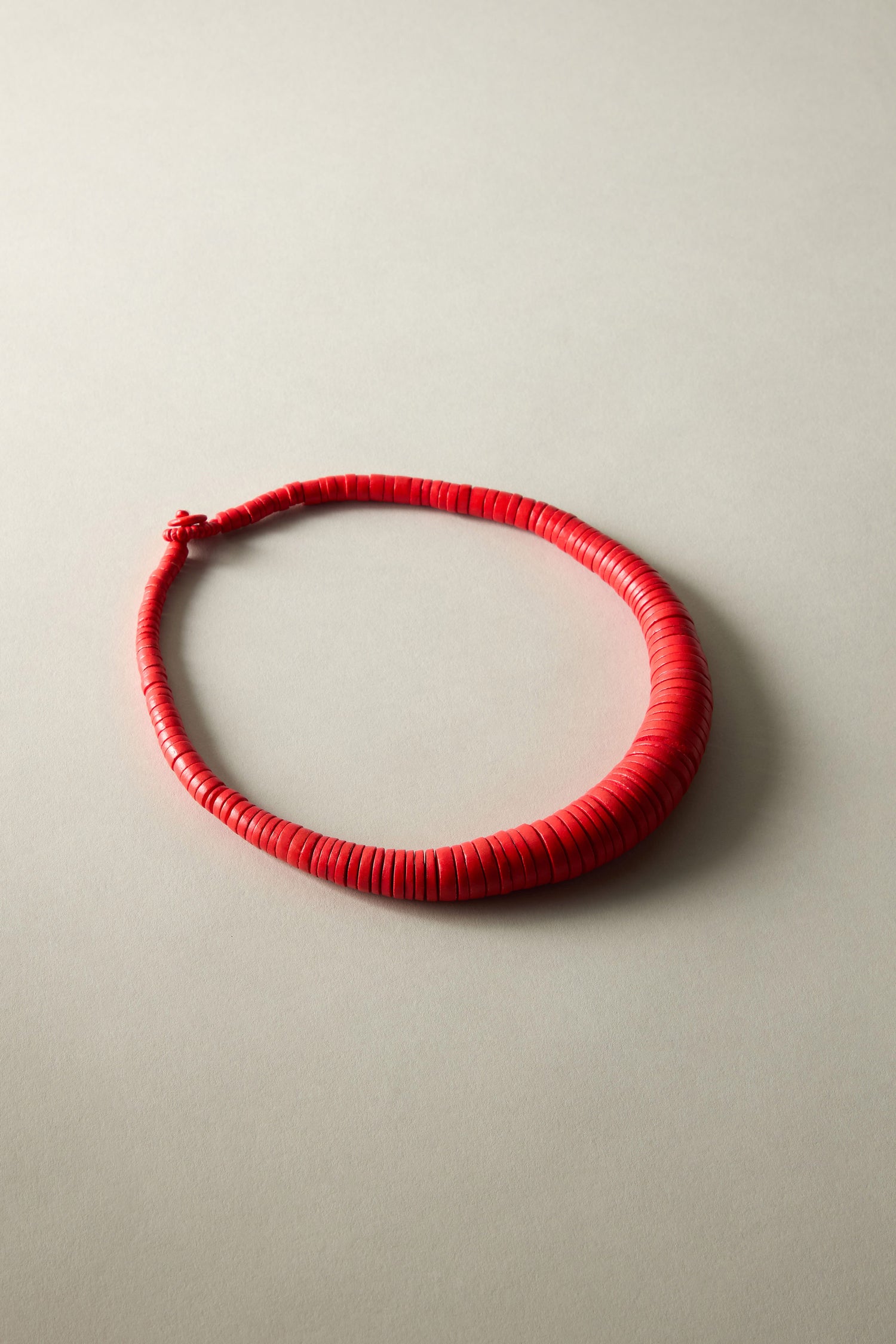 A red, coiled coco disc necklace, similar to a traditional bead necklace, displayed on a neutral light background.