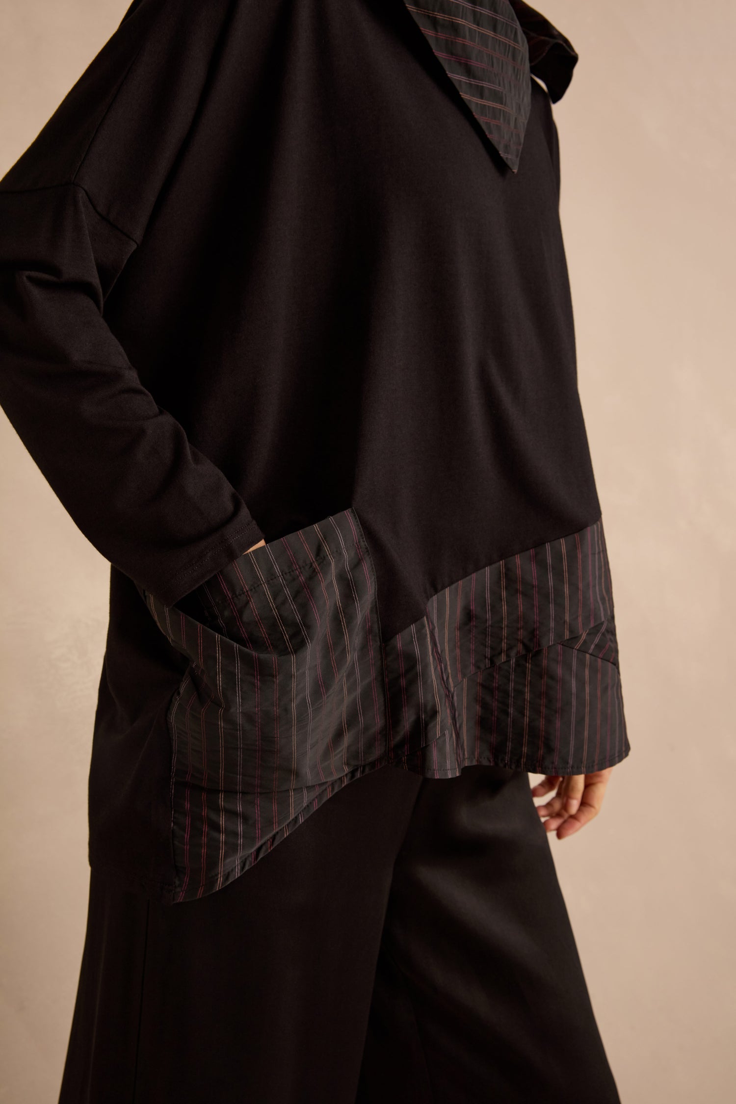 Someone wearing the Stripe Jersey Taffeta Tunic, which features a loose fit and striped fabric accents on the hem and pockets, paired with black pants.