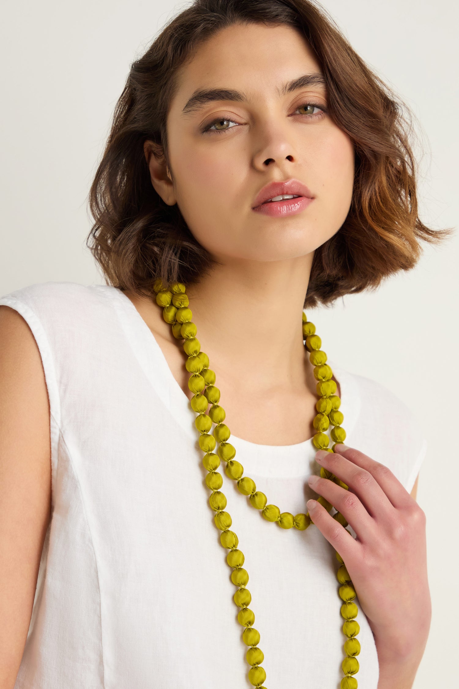 A woman with short brown hair and a white sleeveless top wears the Handmade Long Silk Spheres Necklace in yellow, looking at the camera with a neutral expression.
