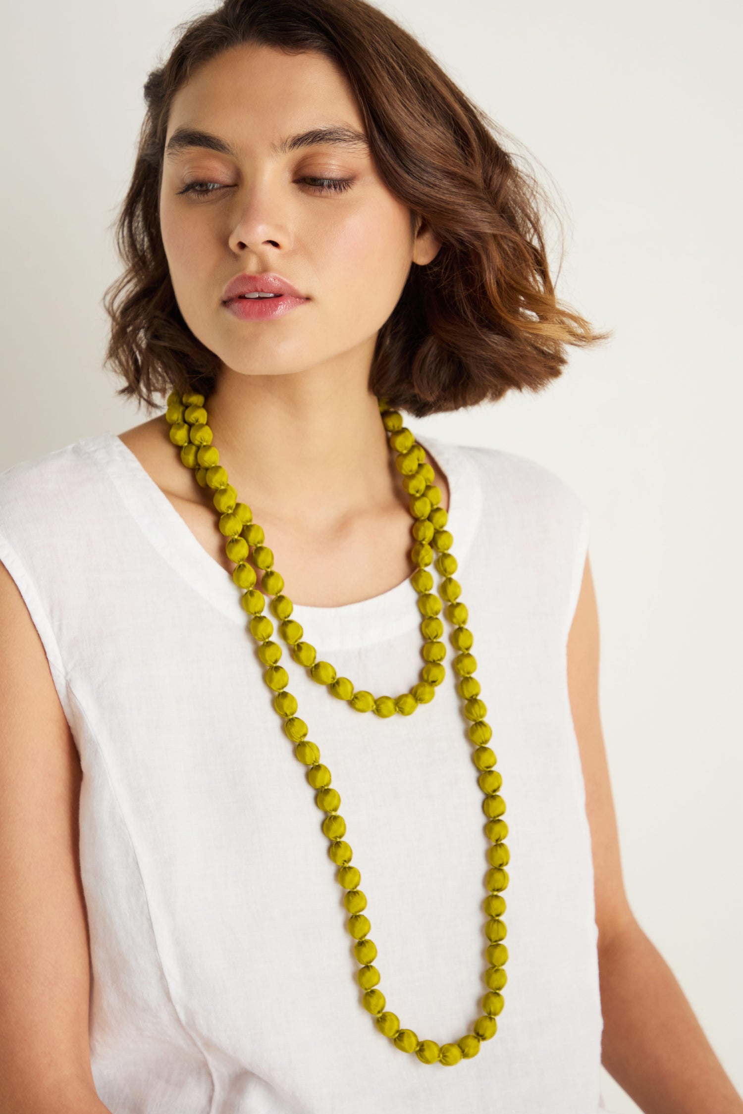 A woman with short brown hair in a white sleeveless top wears two Handmade Long Silk Spheres Necklaces, standing against a plain background.