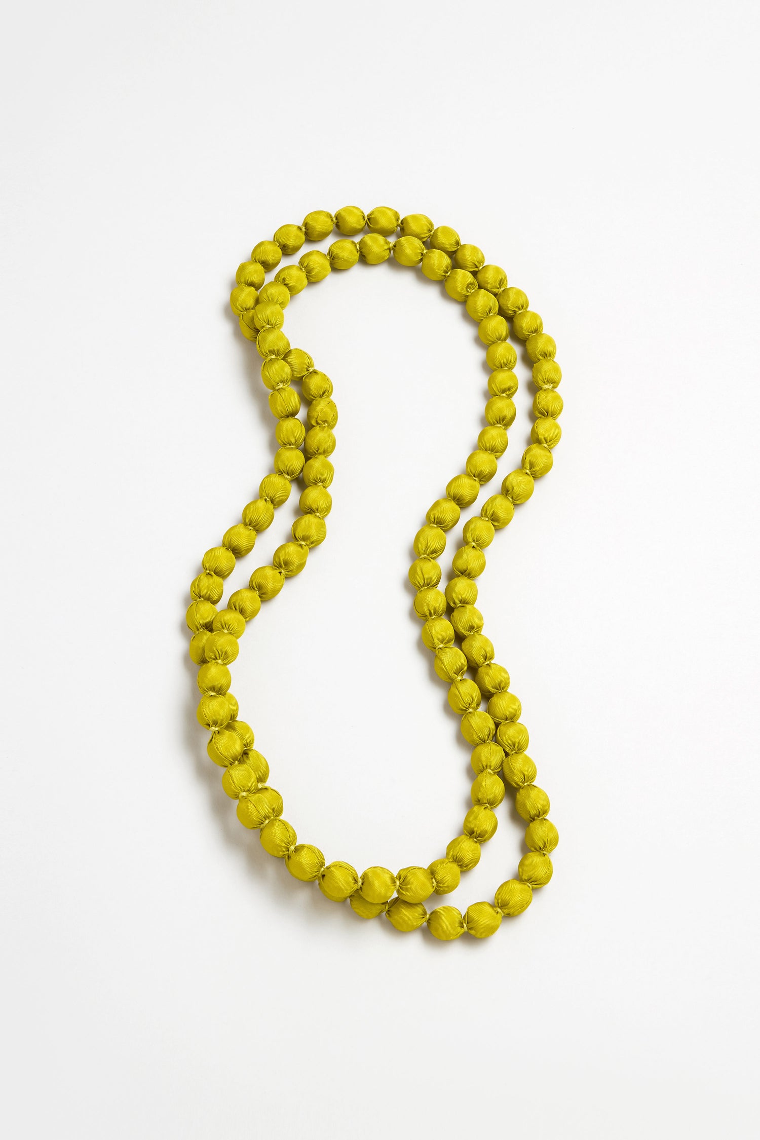 The Handmade Long Silk Spheres Necklace, featuring lightweight double strands of round, yellow-green beads, is artfully arranged in an S-shape on a plain white background to highlight its artisanal design.