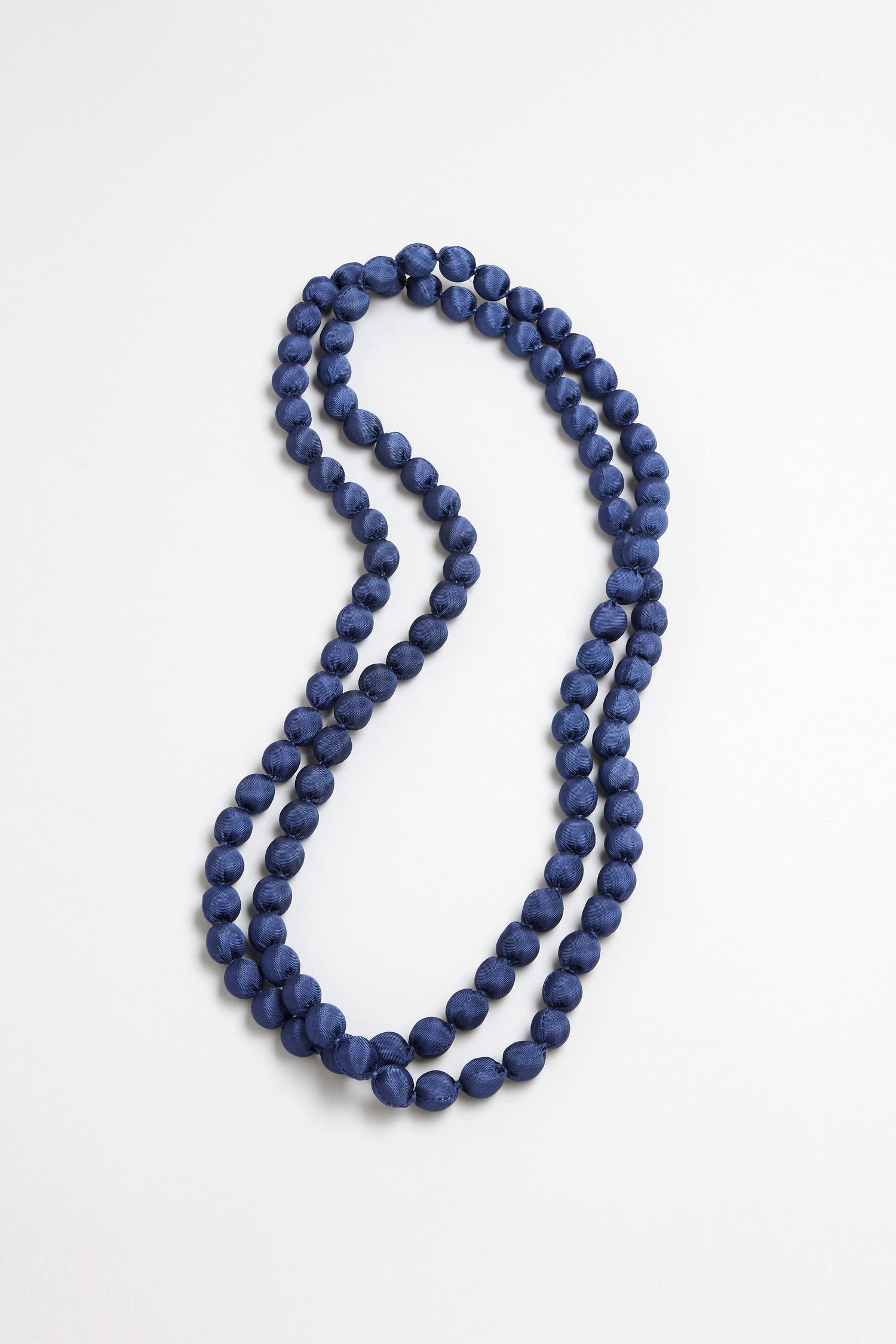 The Handmade Long Silk Spheres Necklace, featuring round dark blue beads, is displayed in a loose double-loop on a plain white surface.