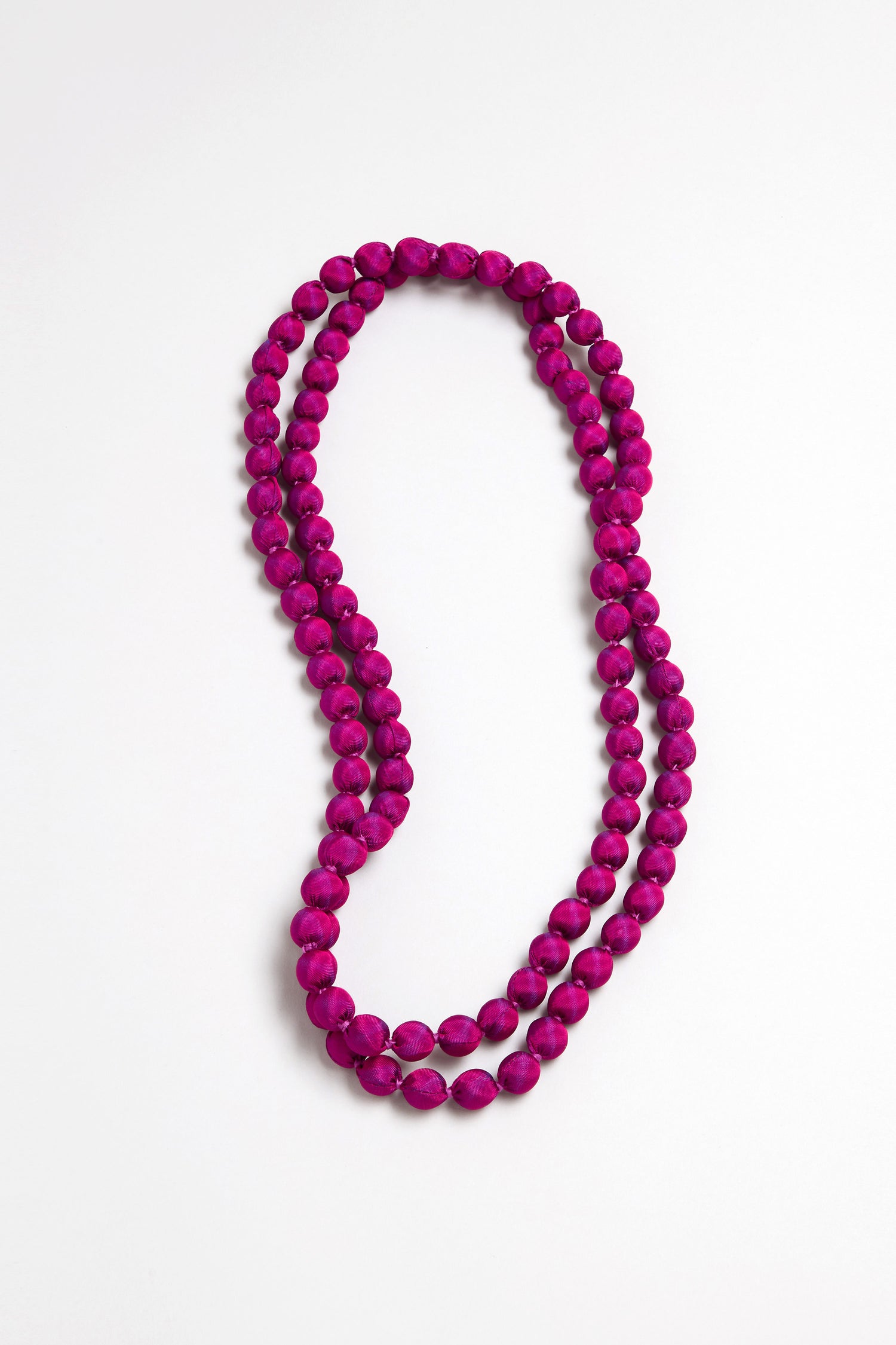The Handmade Long Silk Spheres Fuchsia Necklace is a double-stranded, artisan-crafted piece featuring oval magenta beads, artfully arranged on a white background.
