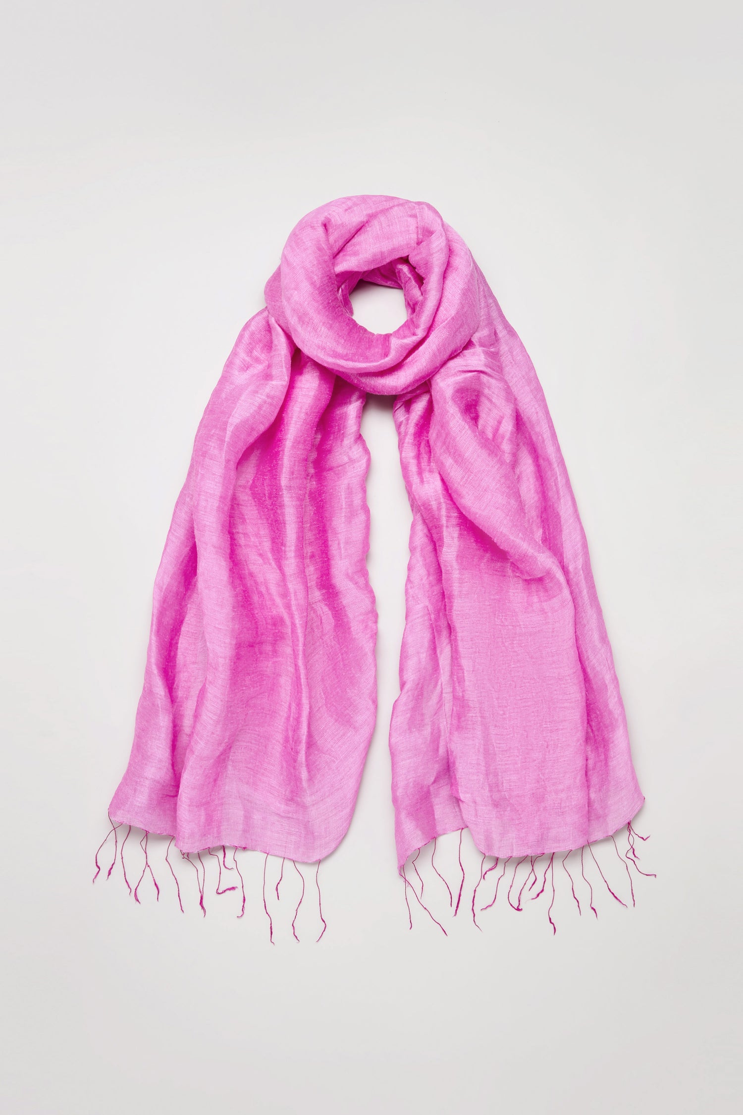 The Soft Linen Fringe Scarf in bright pink features a crinkled texture and fringed ends, shown laid flat on a light background—ideal for lightweight layering.
