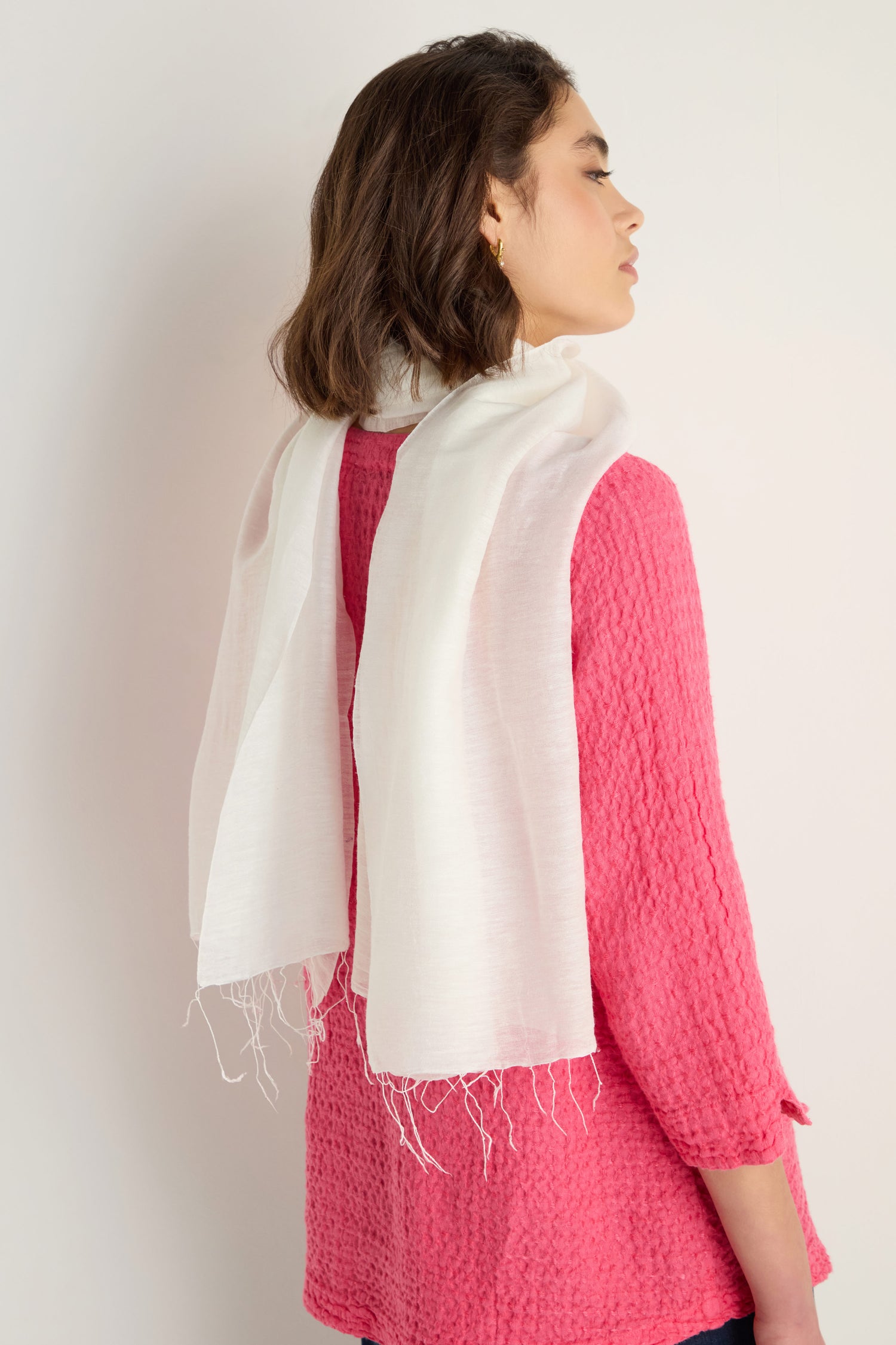 A woman with short brown hair wears a textured pink top and the Soft Linen Fringe Scarf draped over her shoulders against a plain light background—perfect for lightweight layering.