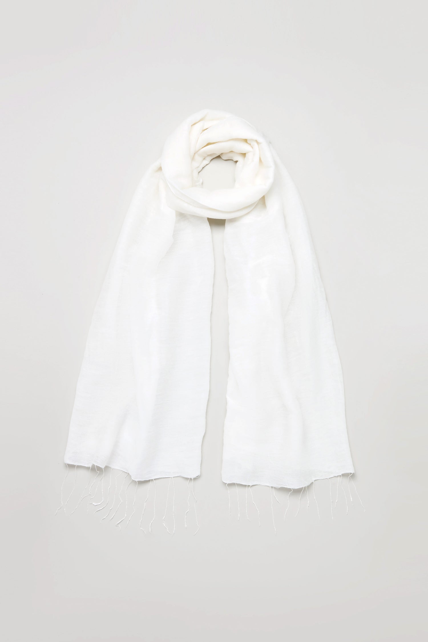 The Soft Linen Fringe Scarf, featuring a plain white hue, soft texture, and fringed ends, is ideal for lightweight layering and shown laid flat on a light grey background.