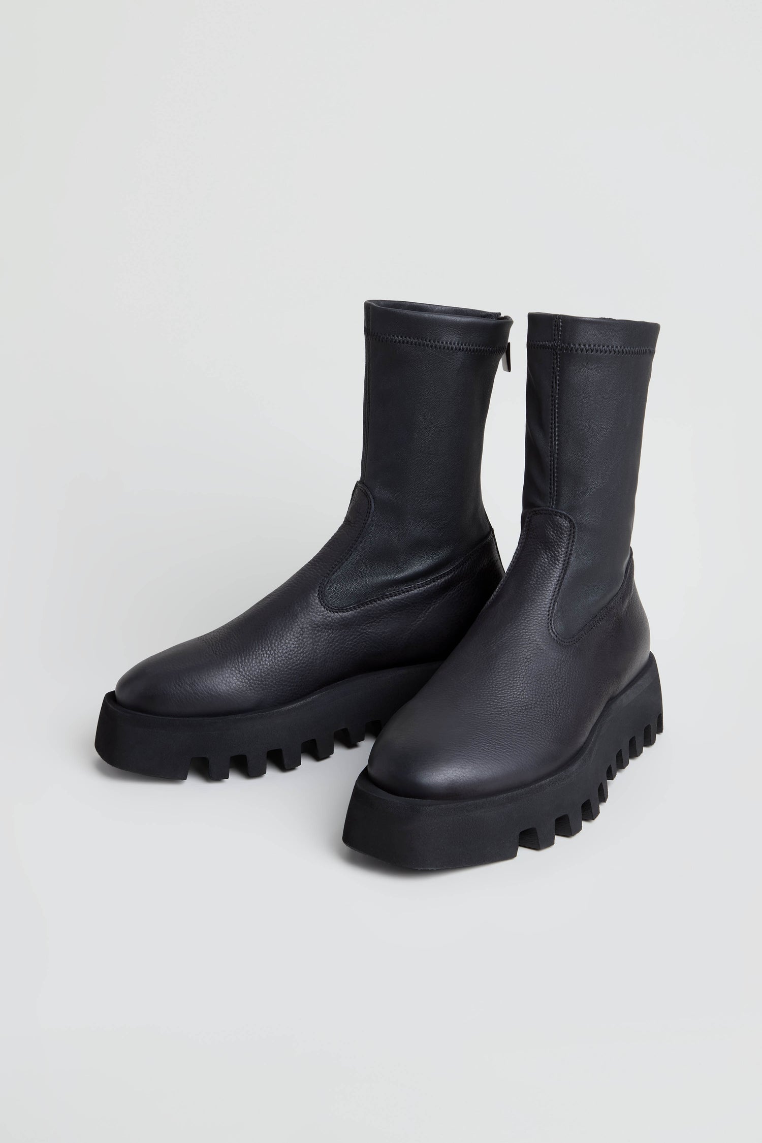 A pair of Platform Napa Leather Stretch Boots in black, featuring a mid-calf height, chunky cleated platform sole, and thick ridged design, displayed on a plain light background.