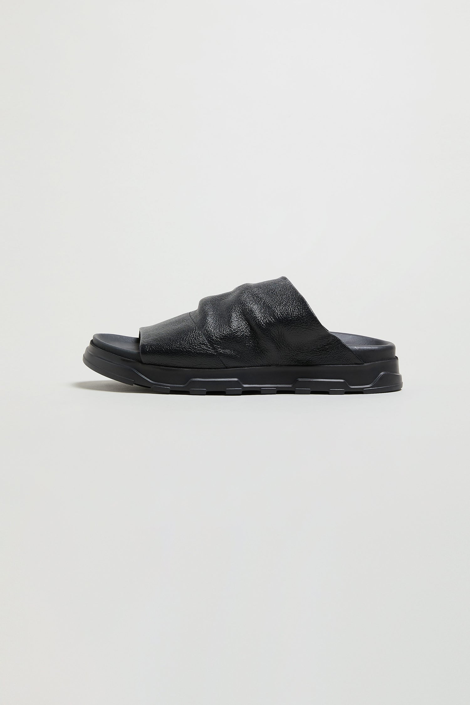 The Crushed Metallic Leather Sliders are black, textured slide sandals with a thick sole, open toe, and ruched metallic leather detailing, shown in profile against a plain light background.
