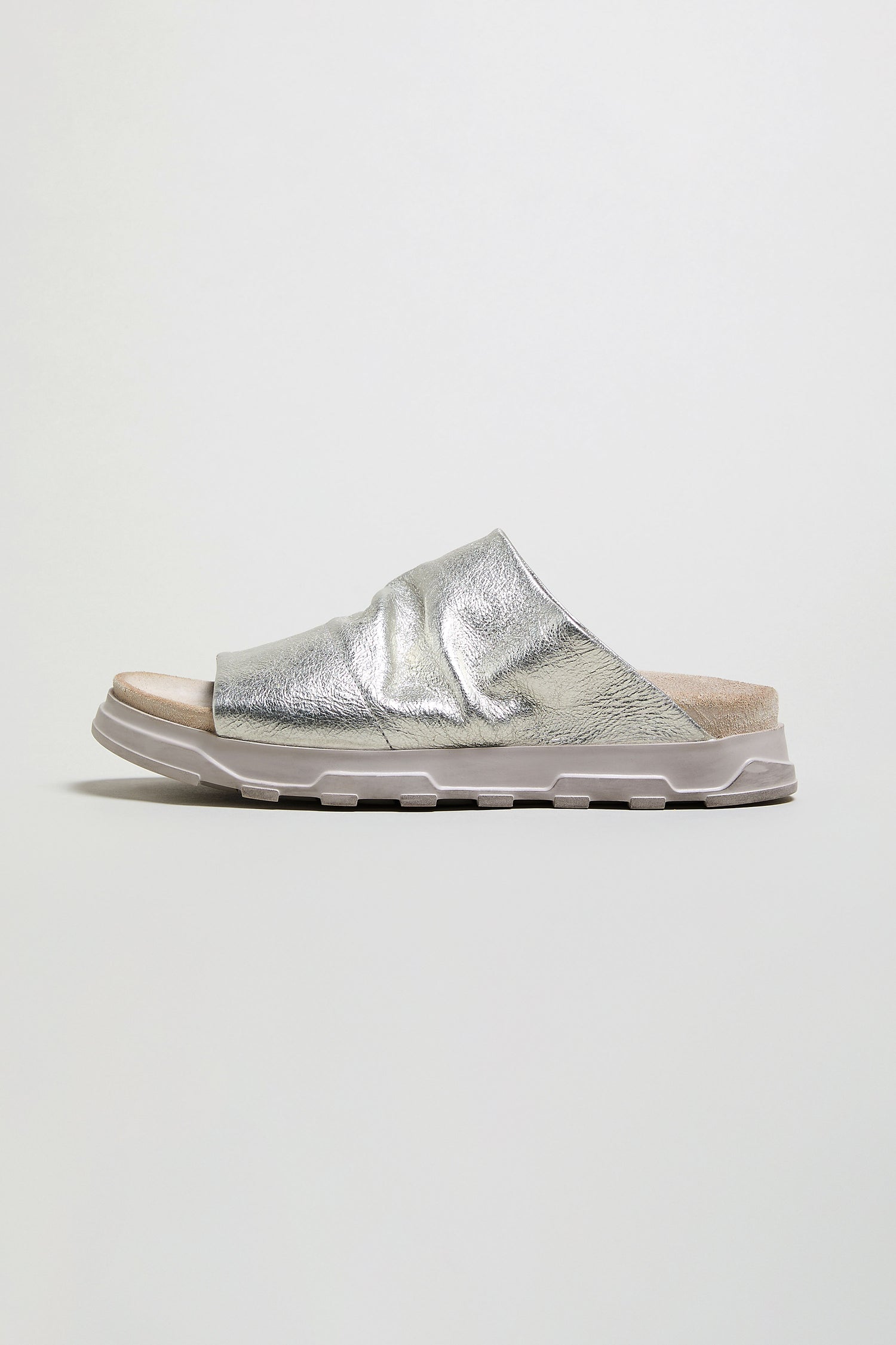 The Crushed Metallic Leather Sliders feature a single silver, textured strap and a flat, light gray sole, displayed in profile against a plain background.