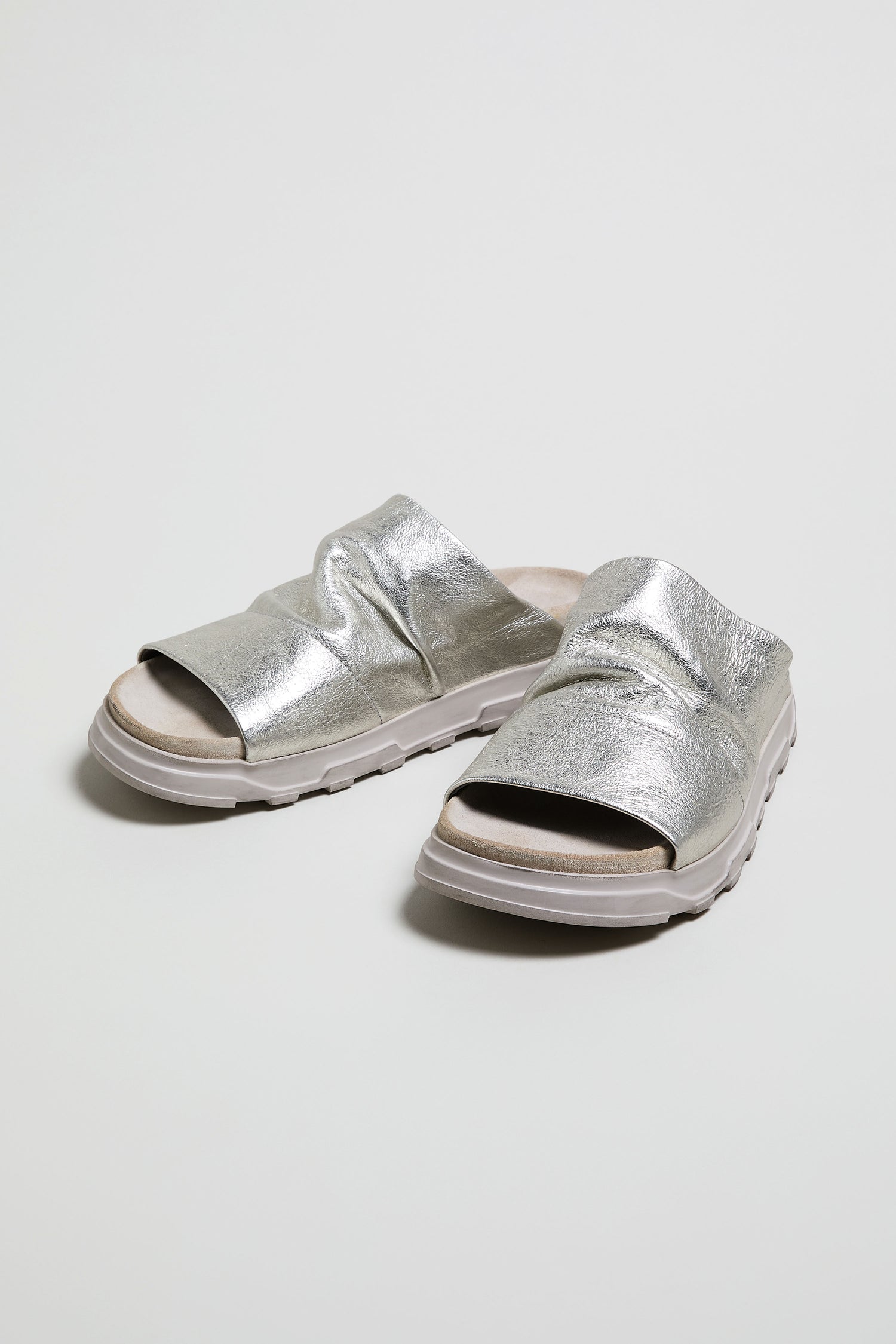 The Crushed Metallic Leather Sliders are women's luxury sandals handcrafted in Italy, featuring crushed metallic leather, thick textured soles, and open toes, displayed on a plain white background.