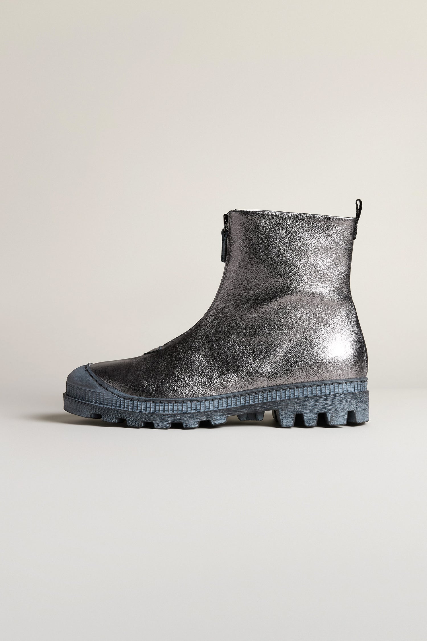 Displayed against a plain light background, the Gunmetal Zip Front Leather Boots feature a metallic silver finish, side zipper, chunky textured sole, and round toe.