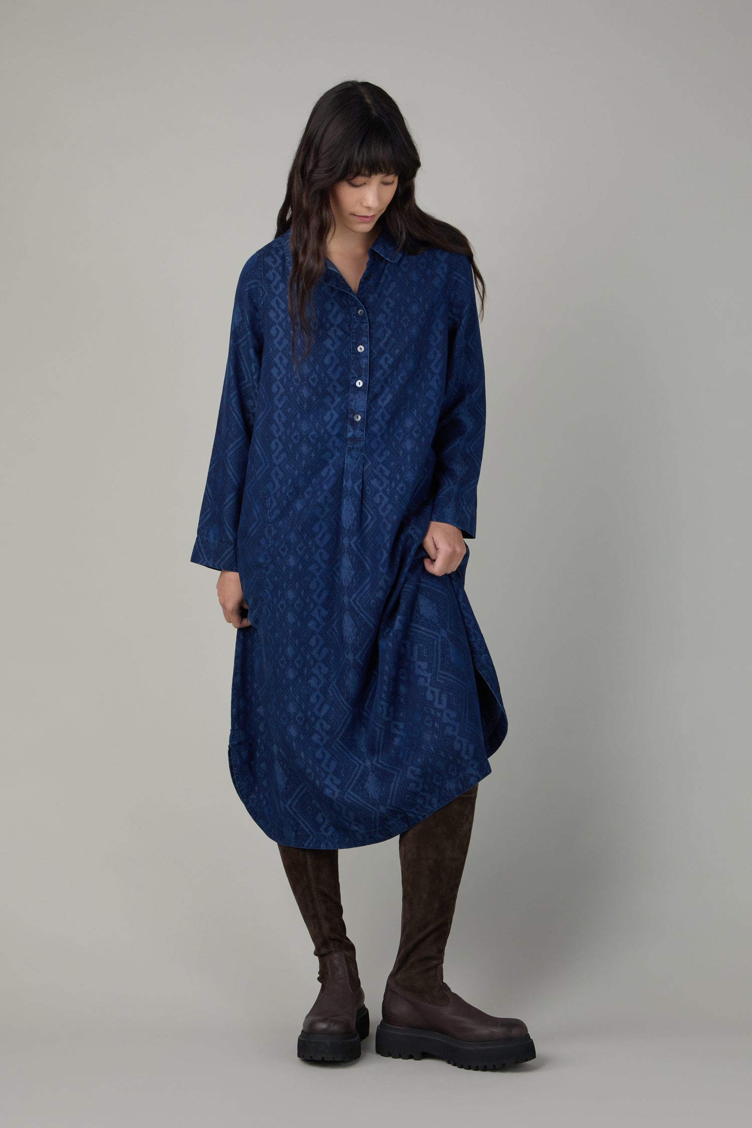 Wearing a loose, long-sleeved blue patterned dress, a person pairs it with Chocolate Long Stretch High Knee Suede Boots featuring a platform sole, standing against a plain grey background.