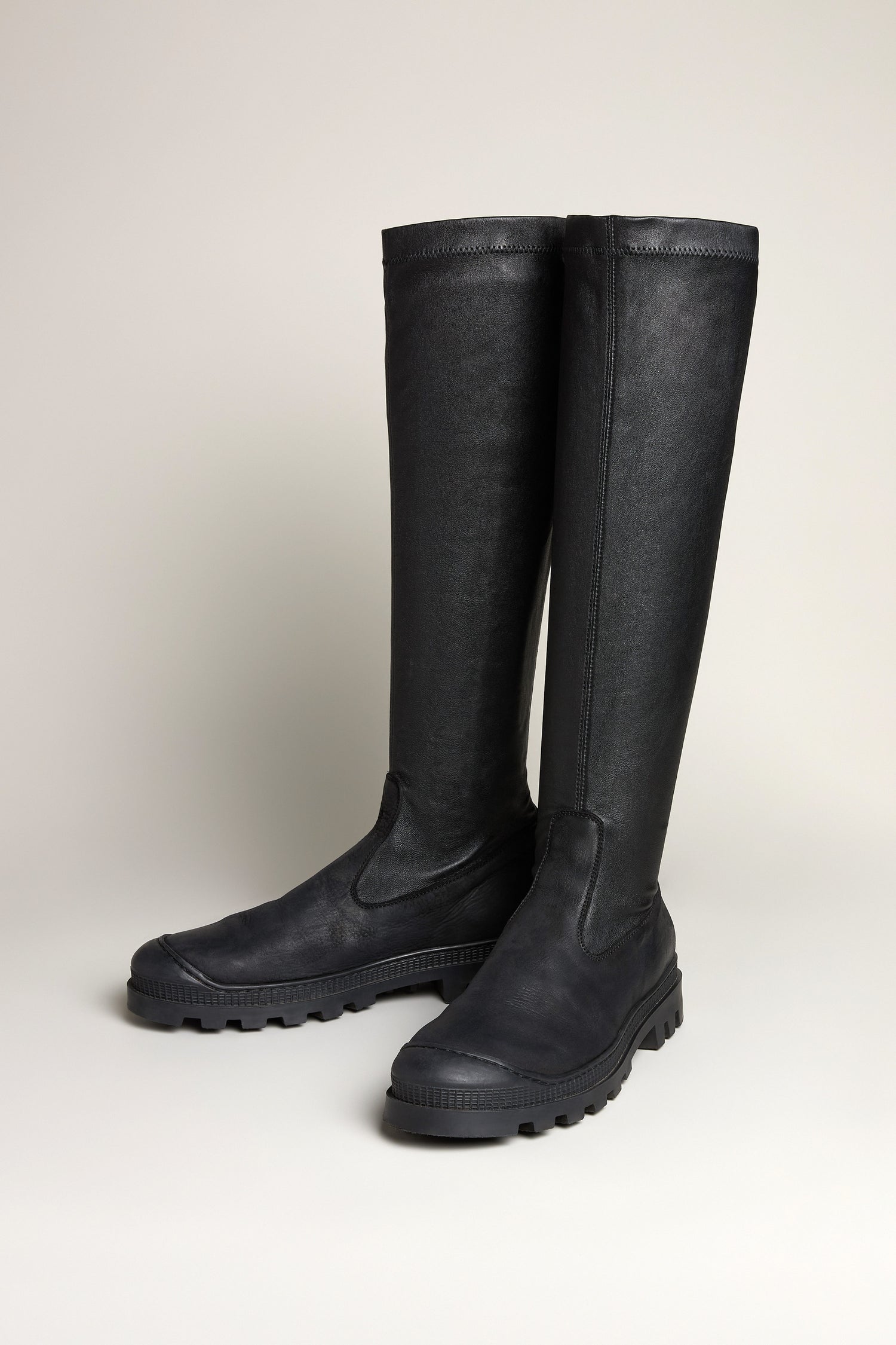 A pair of Stretch Long Nappa Leather Boots with thick black rubber soles stand upright on a light background, highlighting their sleek slip-on design.