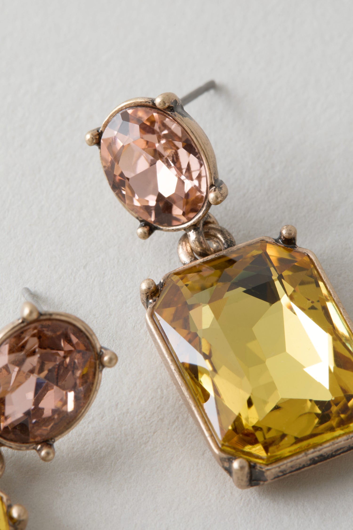 Close-up of Twin Gemstone Earrings showcasing an oval pink gem atop a large rectangular yellow stone, both set in gold-toned metal—modern statement earrings.