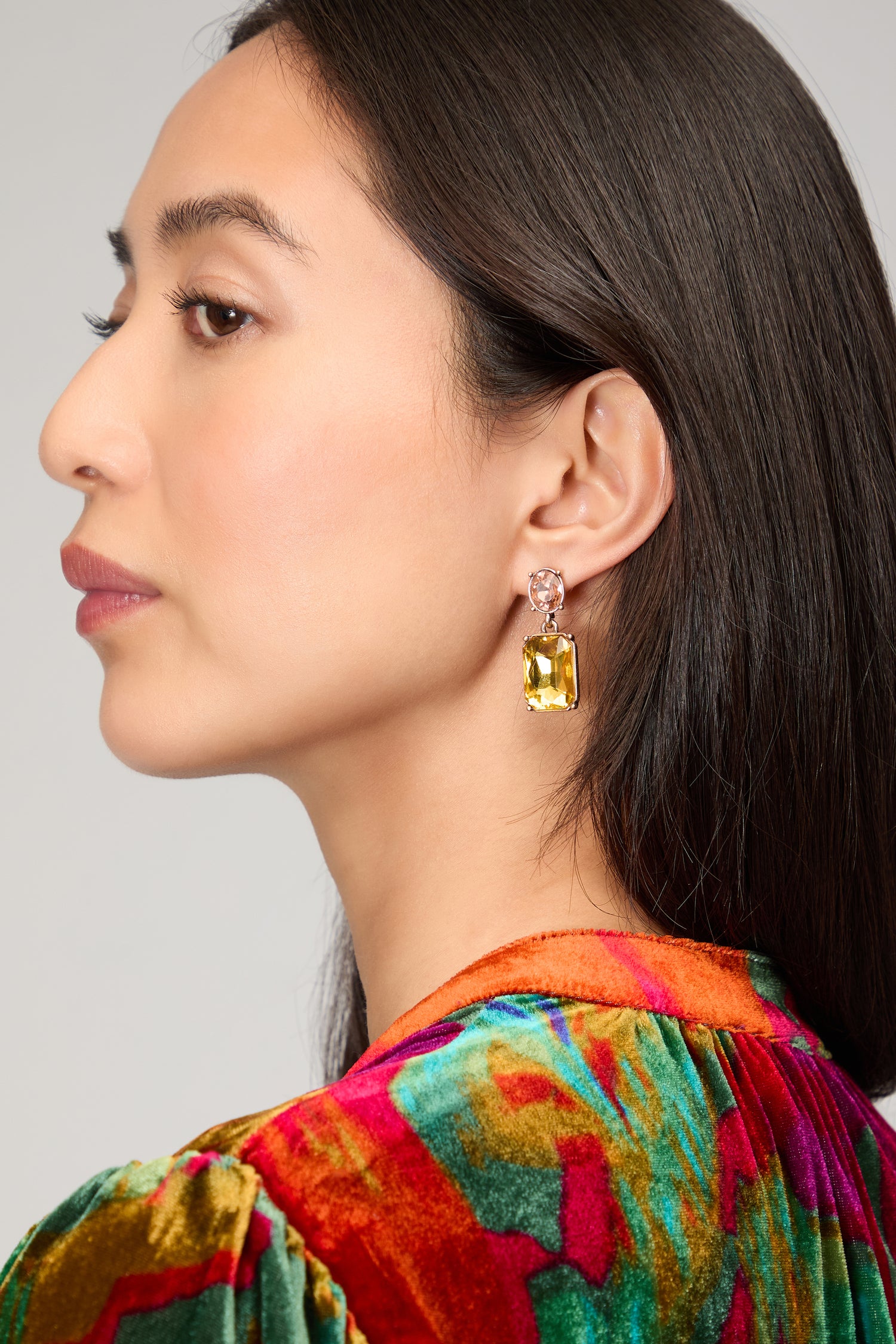 A woman with long dark hair wears colorful velvet and the Twin Gemstone Earrings, each featuring a large yellow stone, shown in profile against a neutral background.