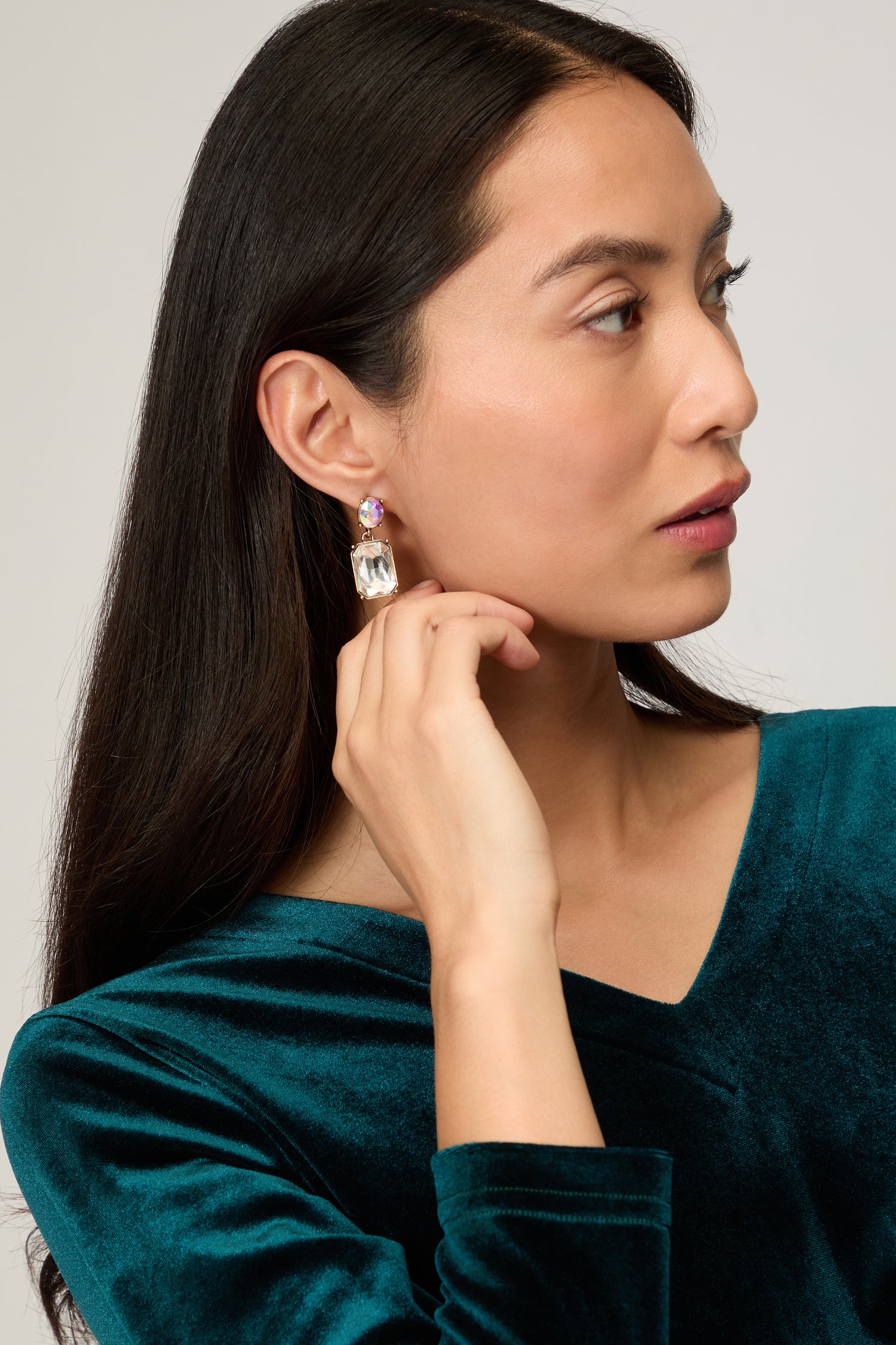 A woman with long dark hair and a green velvet top looks to the side, touching her Twin Gemstone Earrings—modern statement jewelry.