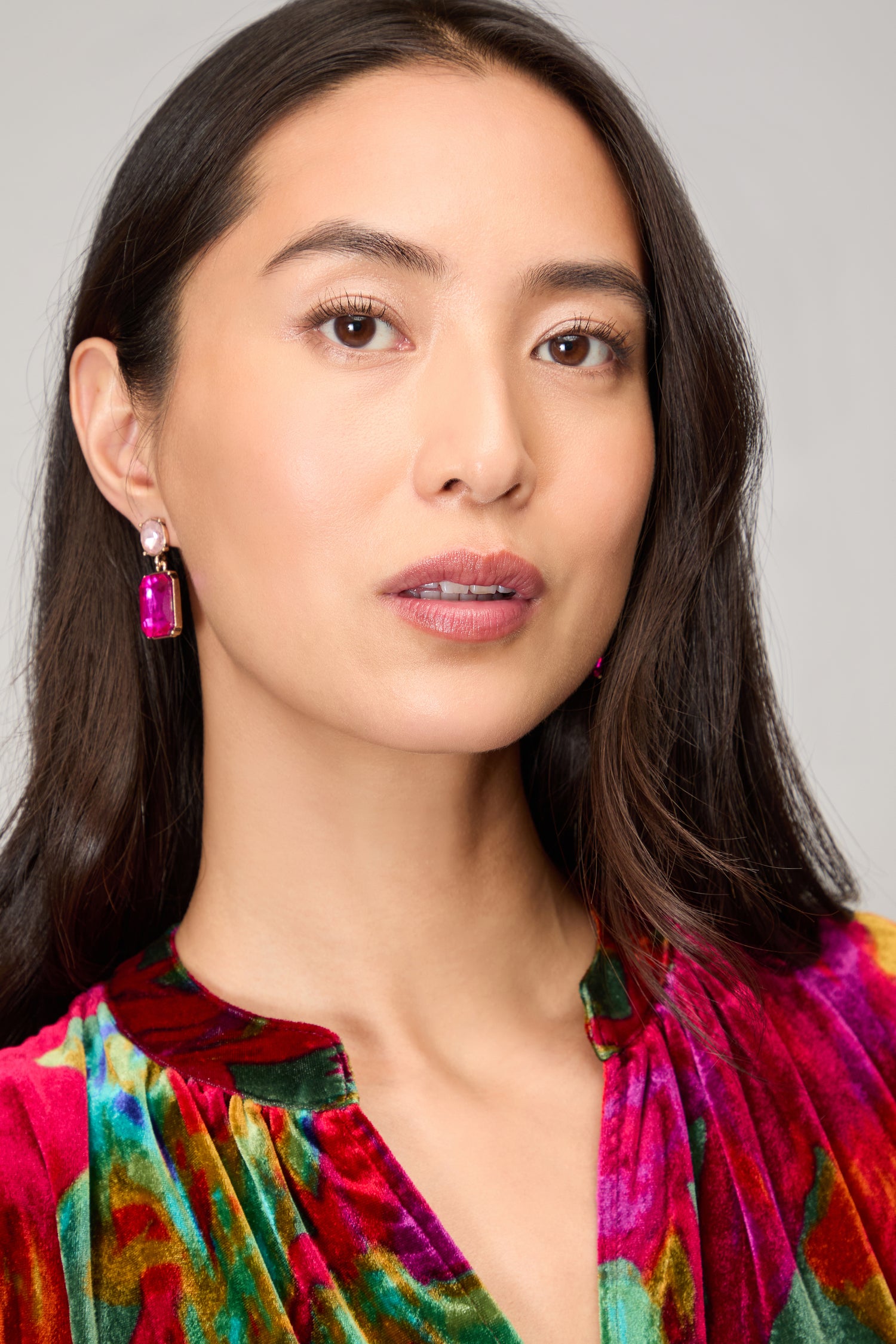 Woman with long dark hair wears modern Twin Gemstone Earrings and a colorful velvet top, gazing slightly to the side against a neutral background.
