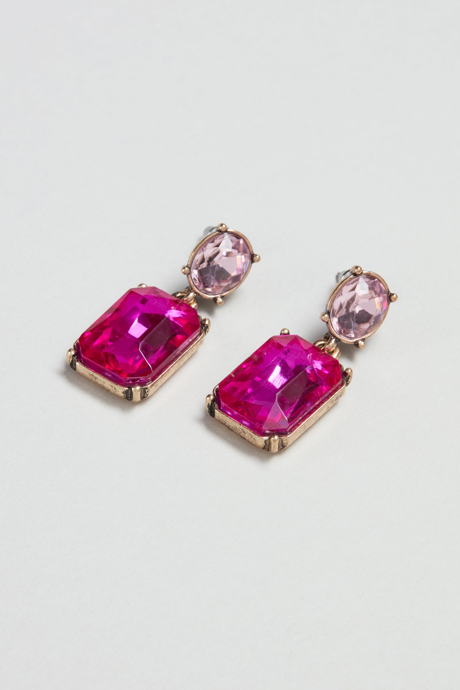 The Twin Gemstone Earrings showcase large rectangular pink gems suspended from smaller oval stones, all set in gold-toned metal for a modern, eye-catching look.