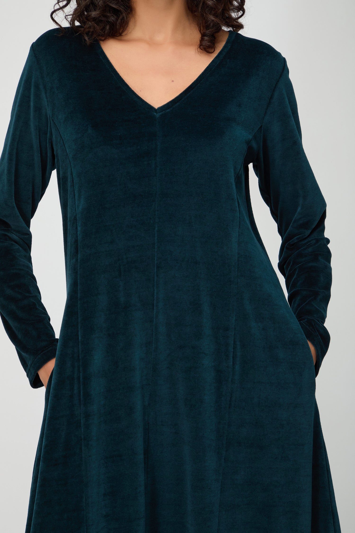 A person wearing a dark teal V Neck Velvet Jersey Bubble Dress with long sleeves; their head is partially out of the frame.