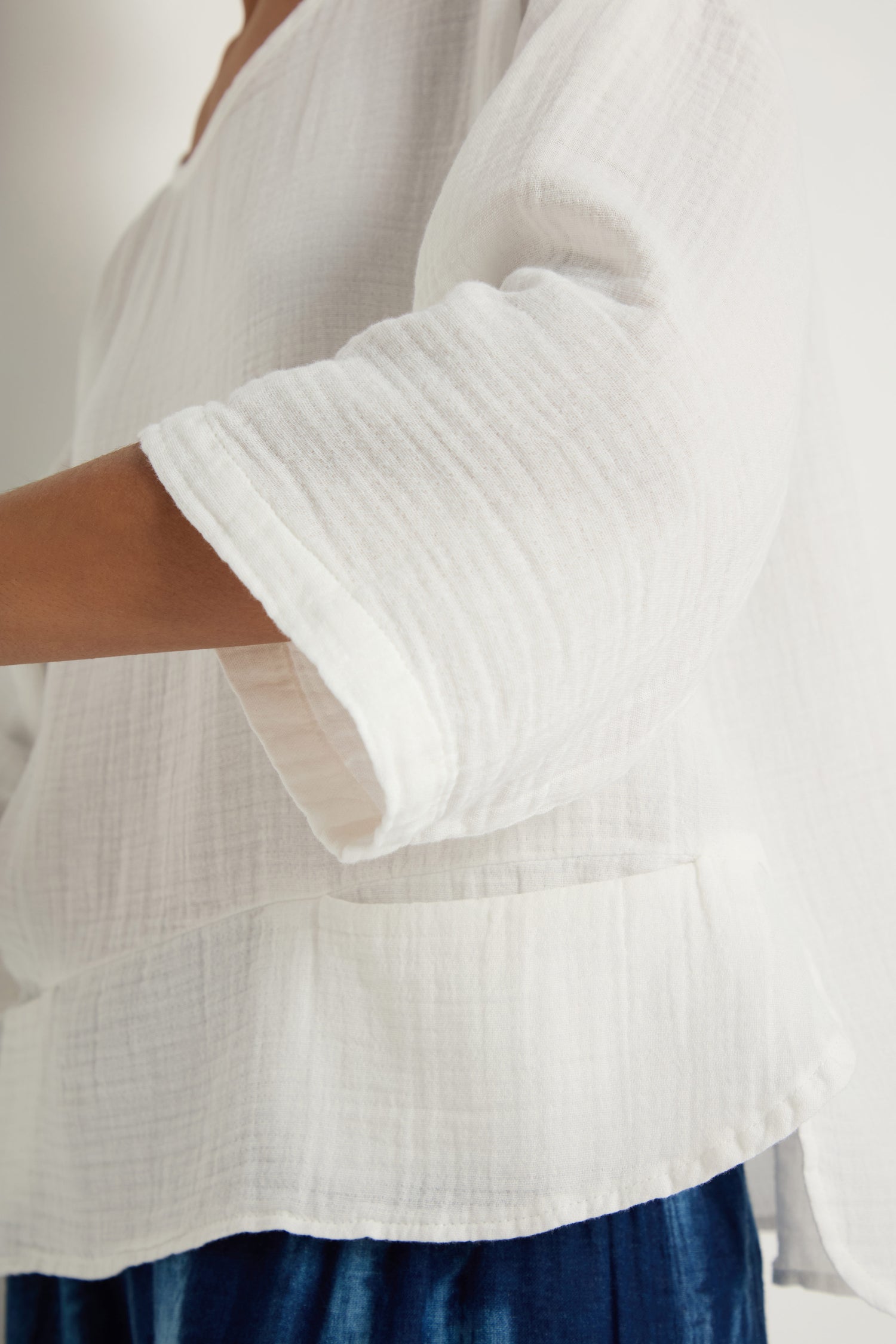 Wearing the Crinkle Two-Pocket Top with wide sleeves and blue bottoms, a person is photographed from the side.