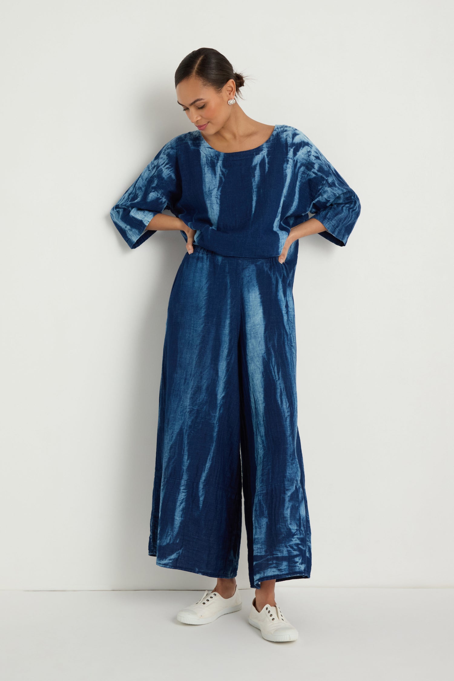 Woman wears Soft Denim Pocket Trousers with a loose-fitting, tie-dye blue top and white sneakers, standing against a plain white background.