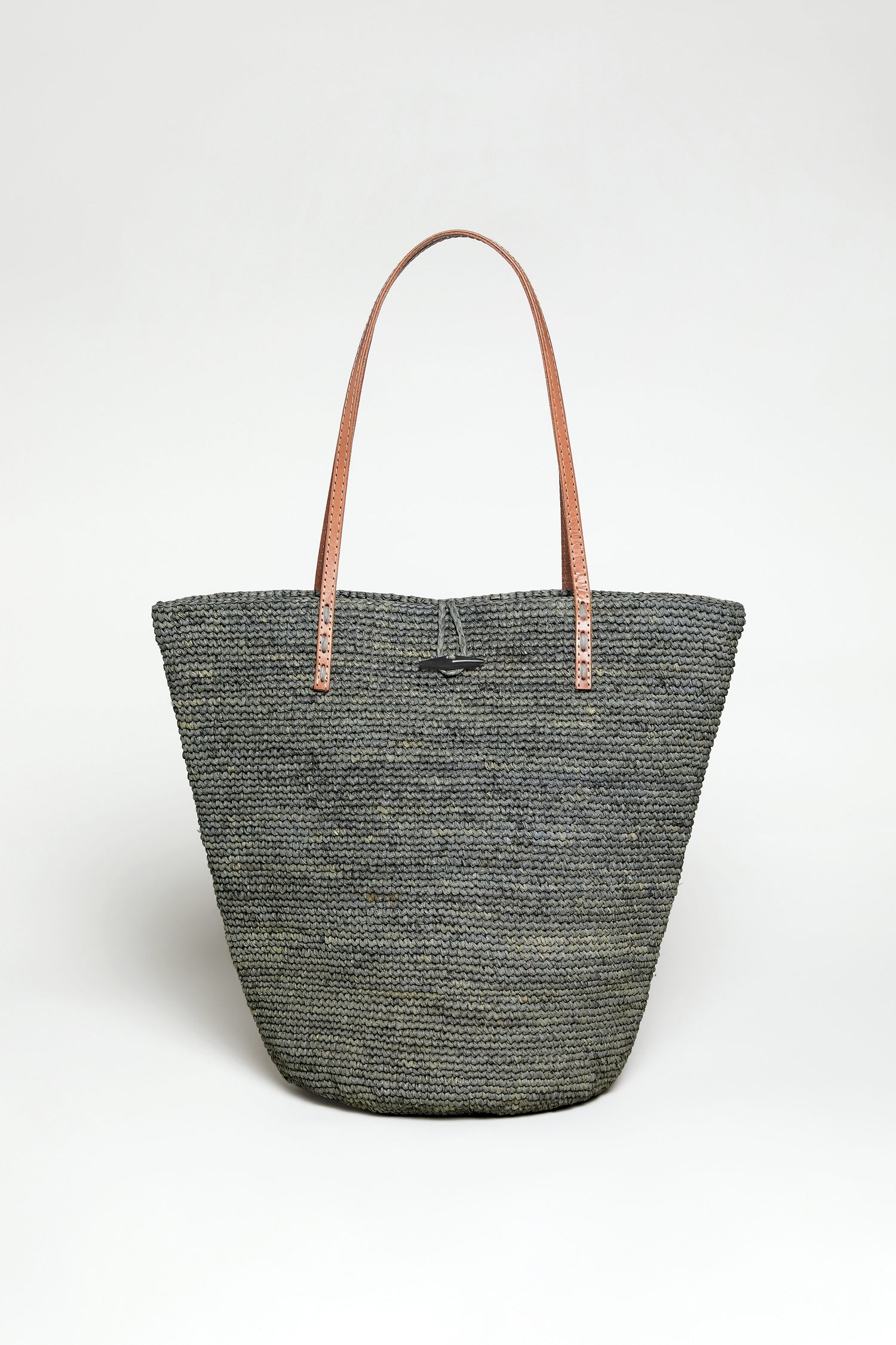 The Ilana Raffia Basket is a large woven gray tote bag with two brown leather shoulder straps, shown upright against a plain white background.