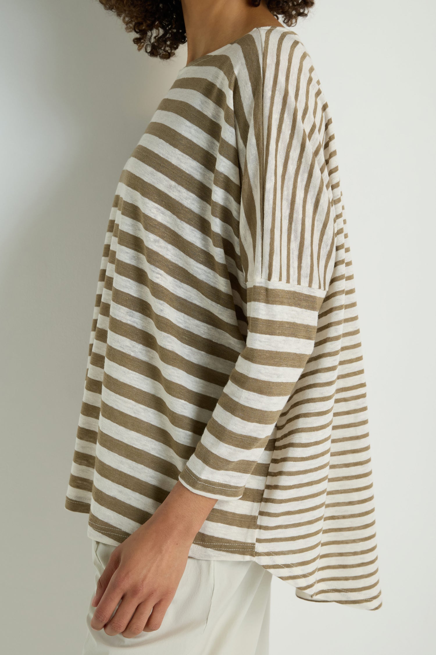 Person wearing an Oversize Stripe Tunic featuring beige and white horizontal and vertical stripes, styled with light-colored pants.