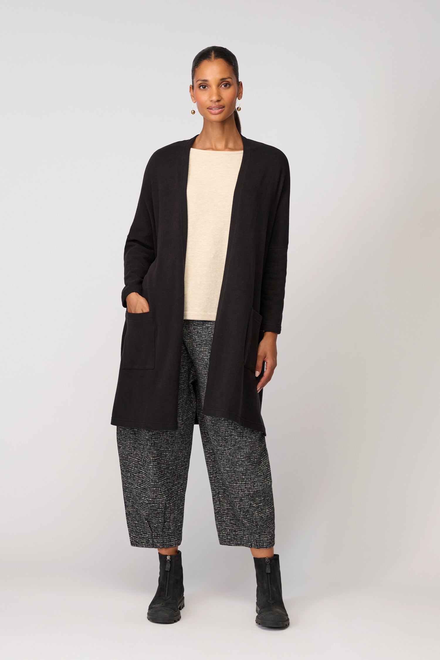 Person standing against a plain background, wearing the Souffle Soft Jersey Cardi as a stylish layering piece over a beige top, paired with gray wide-leg pants and black ankle boots.