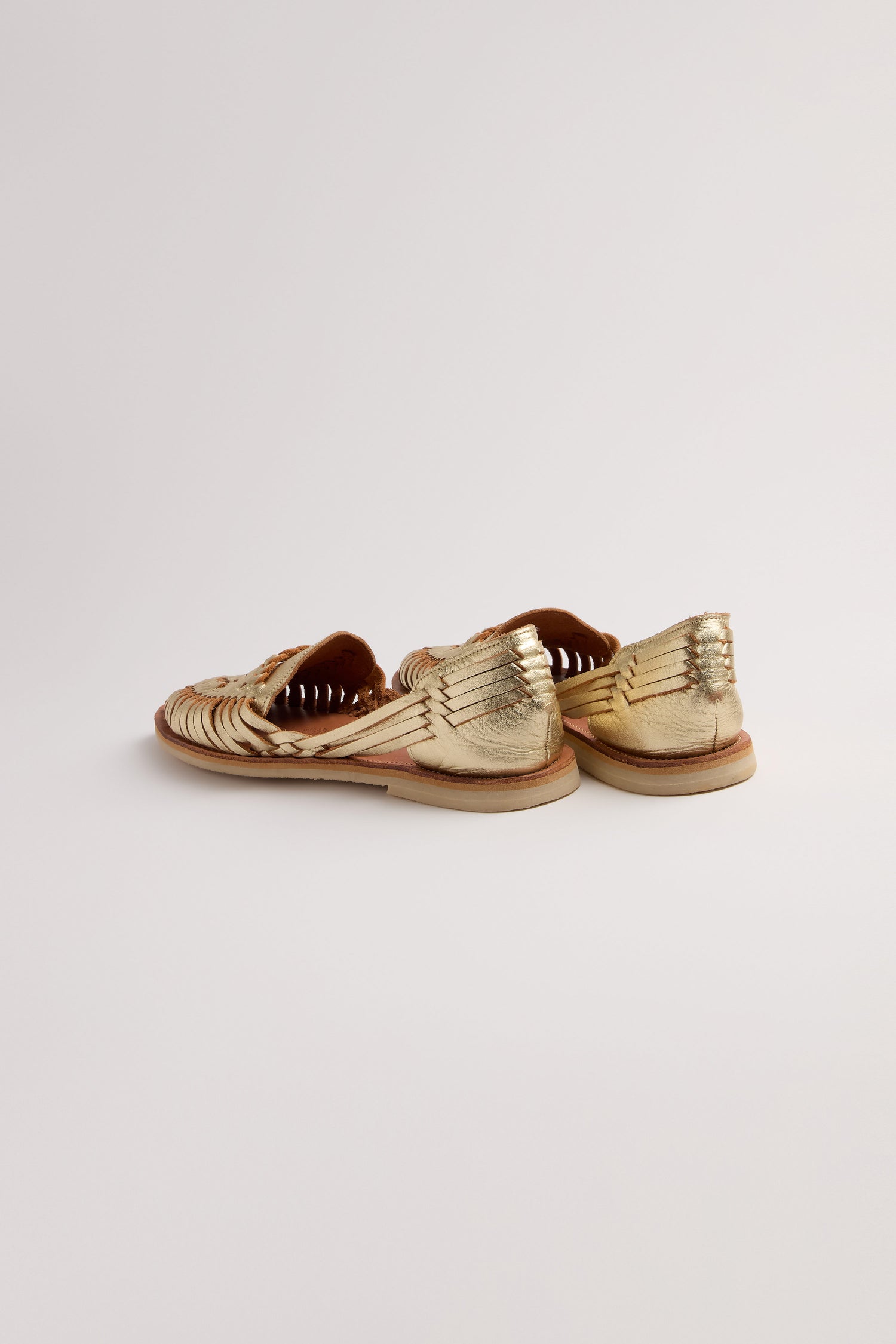 The Gold Alegre Leather Huarache Sandals by Mapache, handcrafted in Mexico from woven leather, are shown on a plain white background, viewed from the back and slightly to the side.