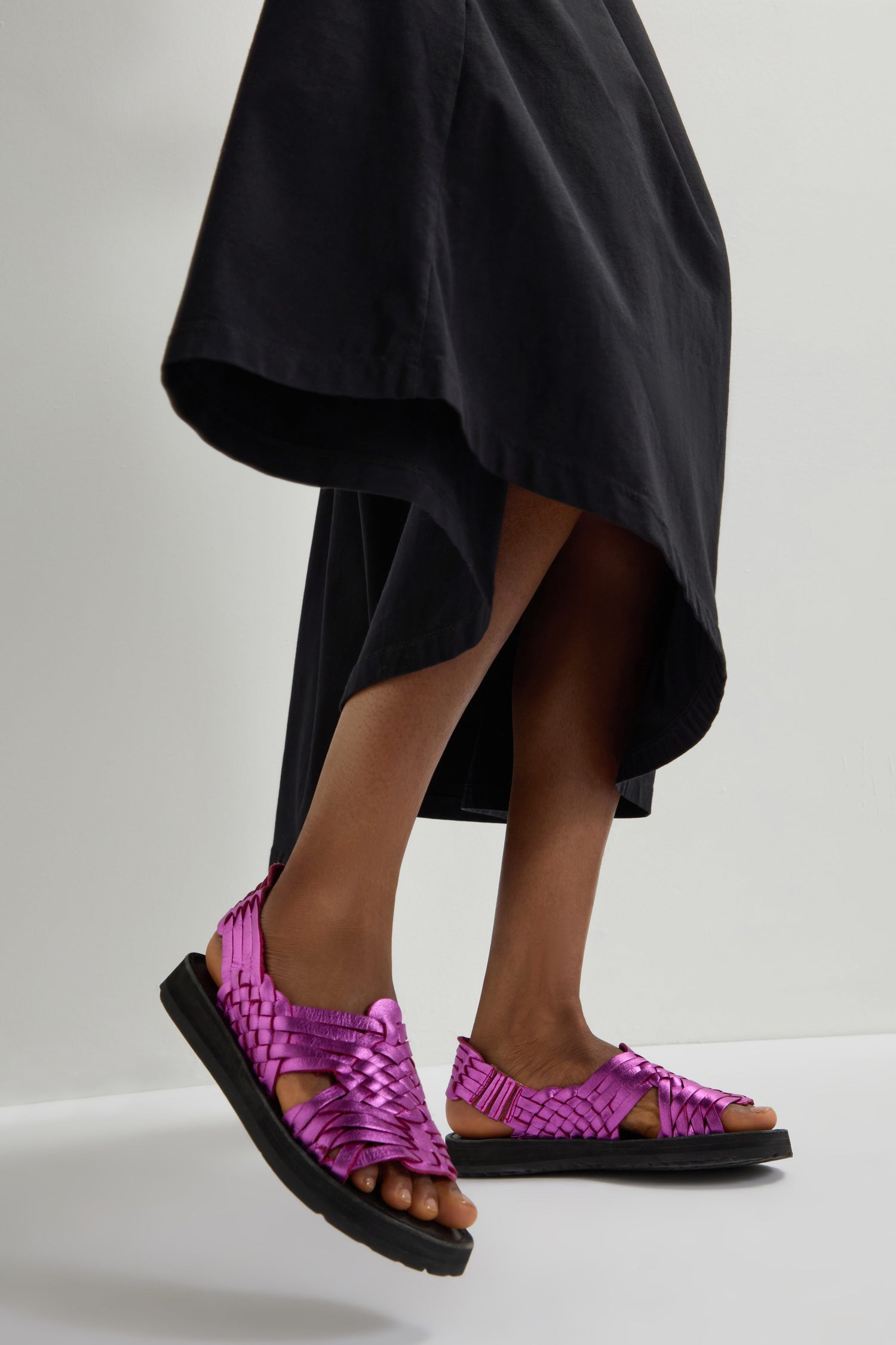 A person in a black skirt and vibrant pink Frida Woven Leather Sandals, handmade in Mexico, stands against a light background.