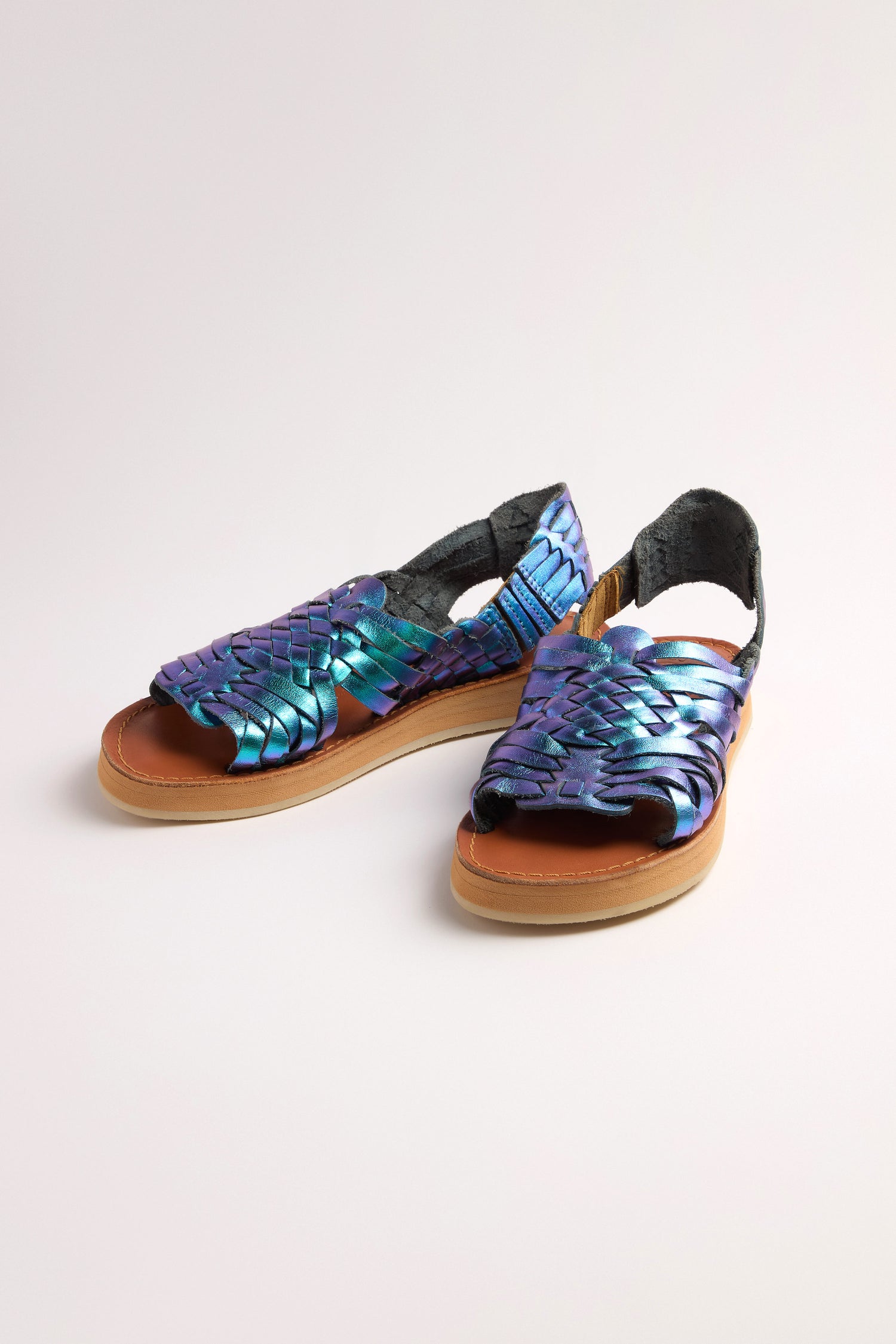 Discover the Frida Woven Leather Sandals, handcrafted in Mexico with an iridescent blue and purple strap design set against a light background and a metallic magenta finish, perfectly blending tradition with modern style.