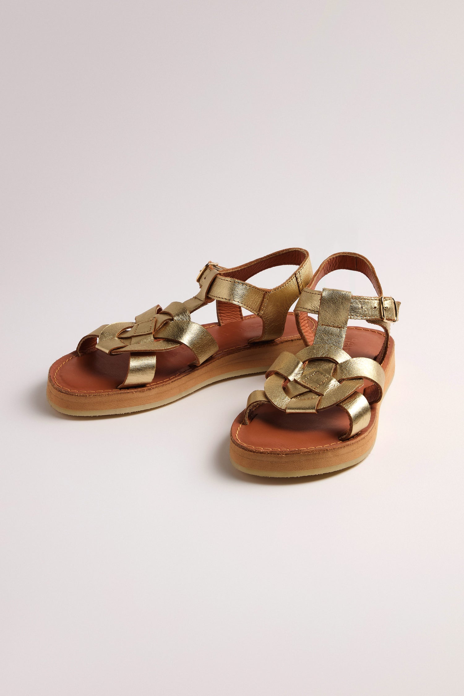 The Tulum Leather Buckle Sandals feature gold metallic woven straps, cushioned soles for comfort, tan leather soles, and handmade premium leather ankle buckles against a neutral background.