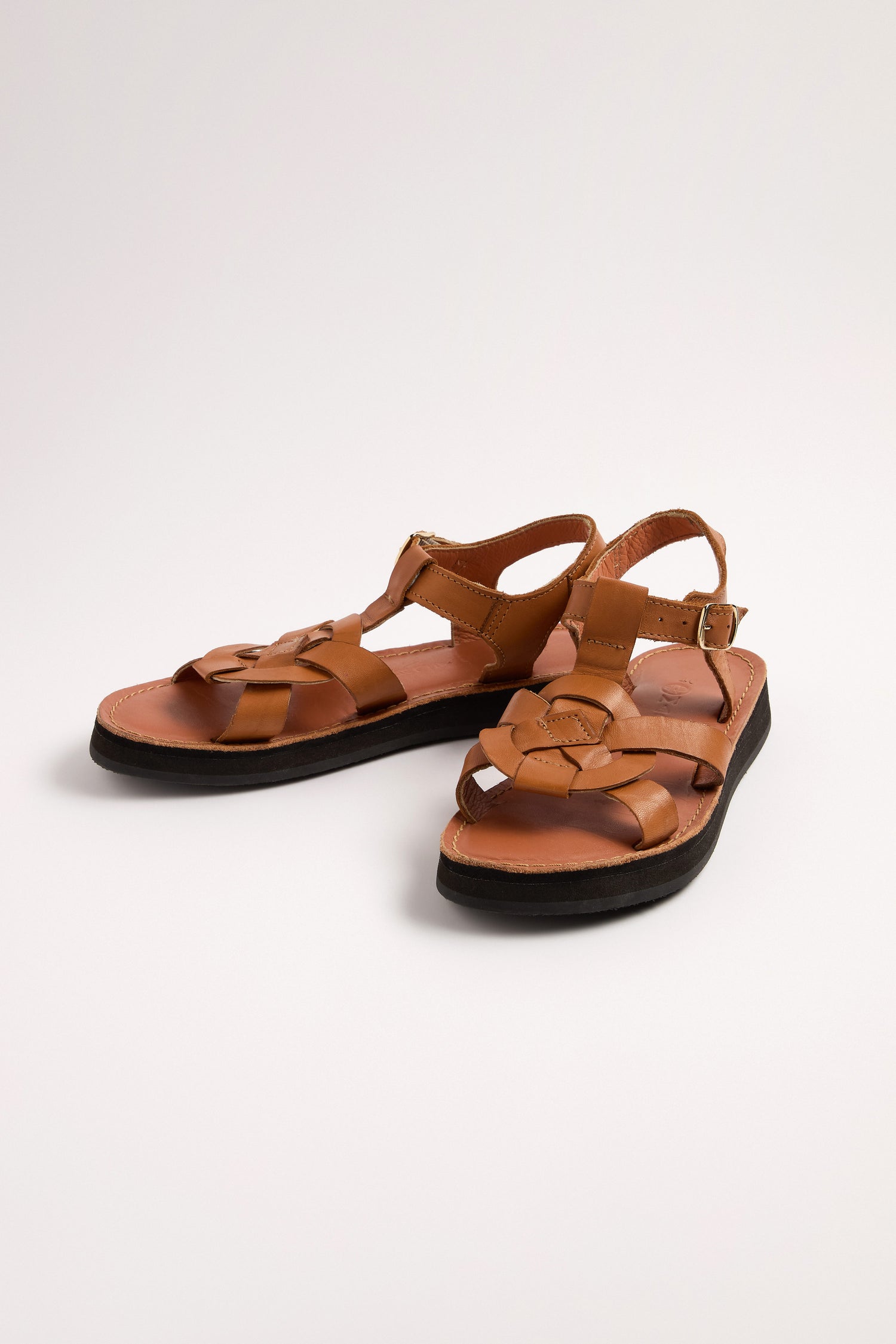 The Tulum Leather Buckle Sandals are handmade with premium brown leather, featuring straps, a buckle closure, cushioned for comfort, and black soles, elegantly placed on a light surface.