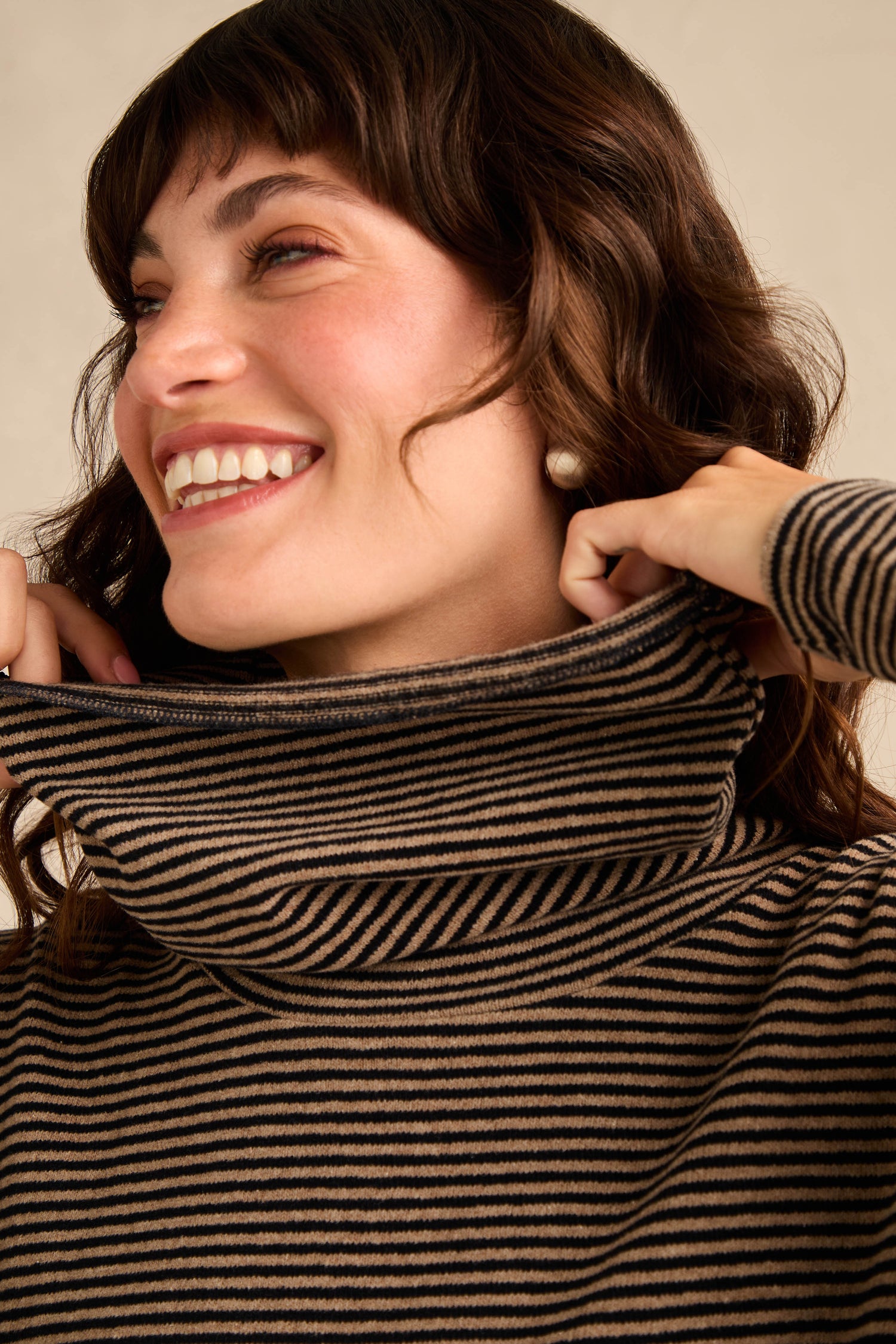 A woman smiles while adjusting the collar of her Roll Neck Narrow Stripe Fleece Tunic.