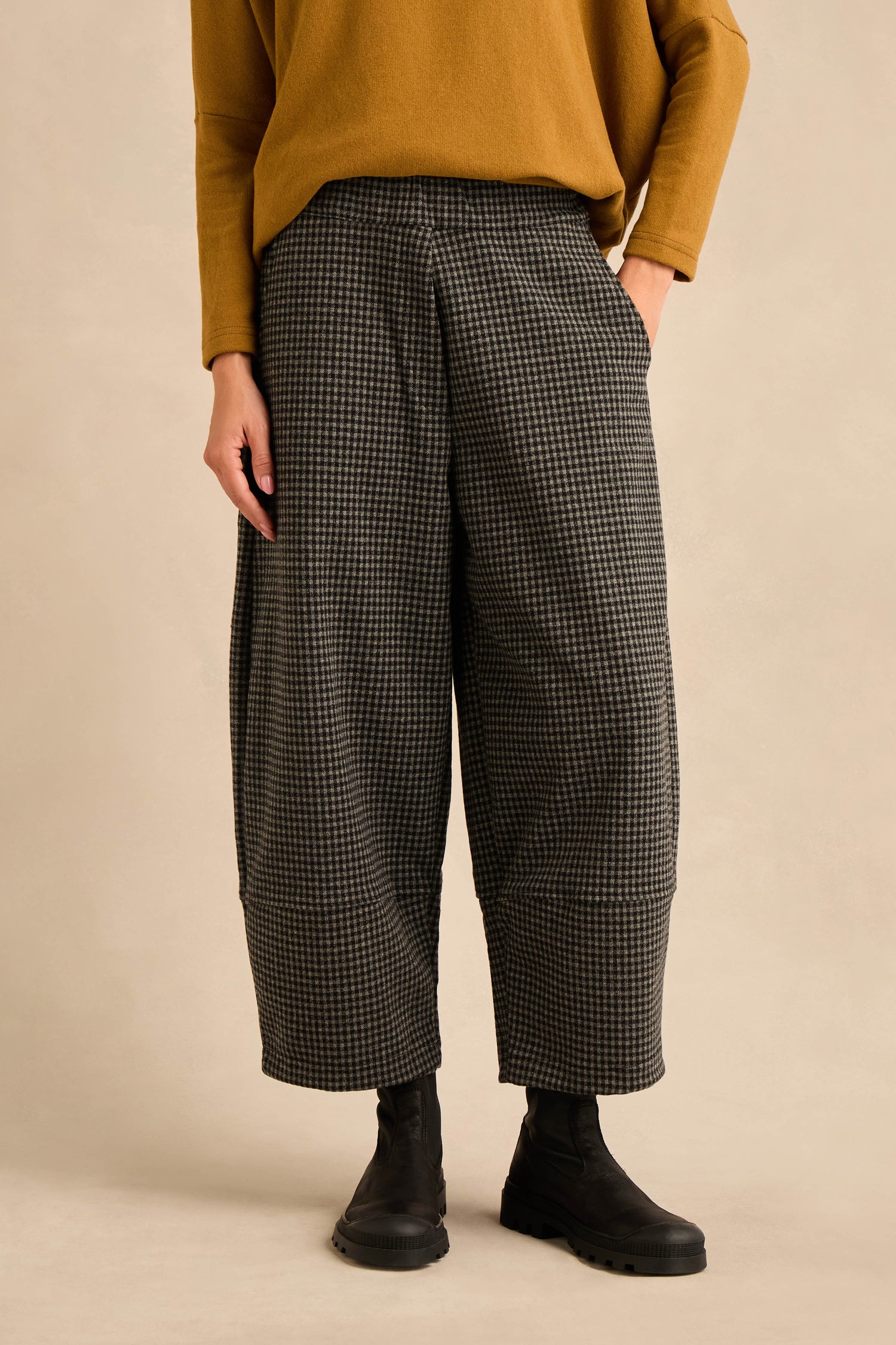 Wearing a mustard long-sleeve top, the person pairs it with Mini Check Jersey Pocket Trousers featuring a cropped leg, and black ankle boots while standing against a beige background.