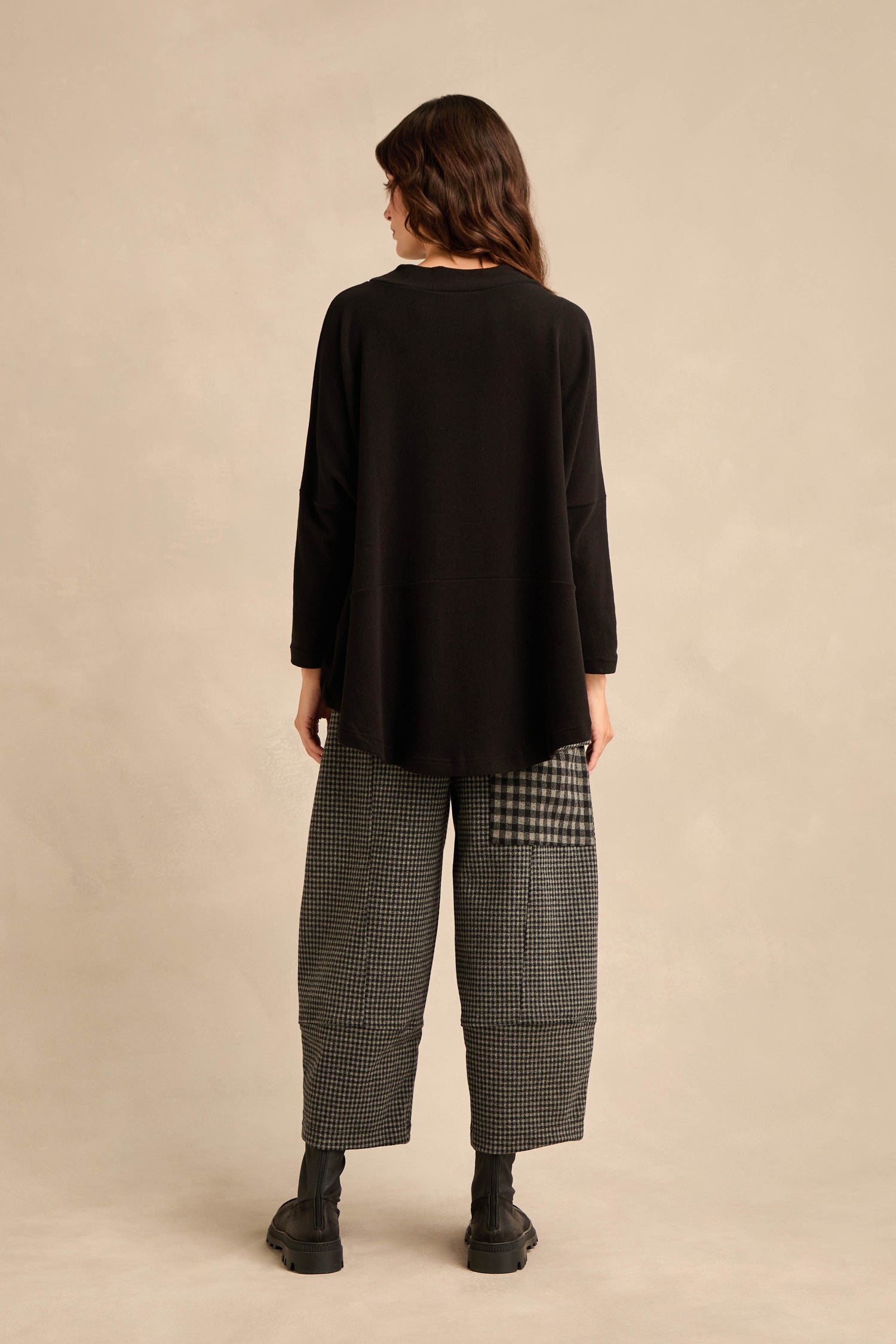A person stands with their back to the camera, wearing the Black Soft Jersey Boxy Top and black-and-white checkered wide-leg pants in a boxy silhouette, paired with black boots against a plain beige background.