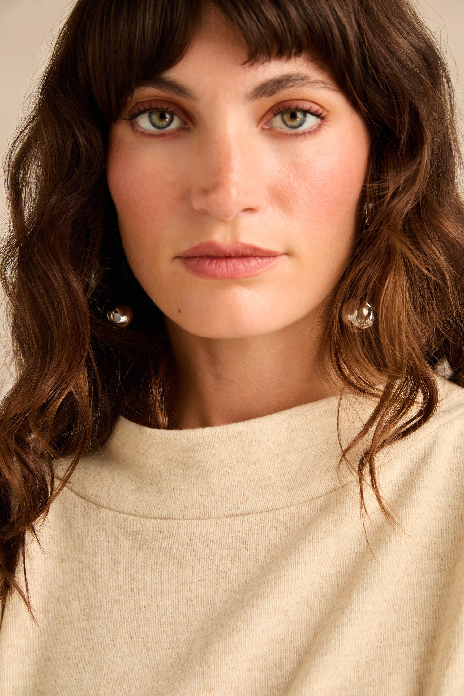 A woman with wavy brown hair, wearing the Cream Marl Soft Jersey Boxy Top and silver ball earrings, looks directly at the camera with a neutral expression.