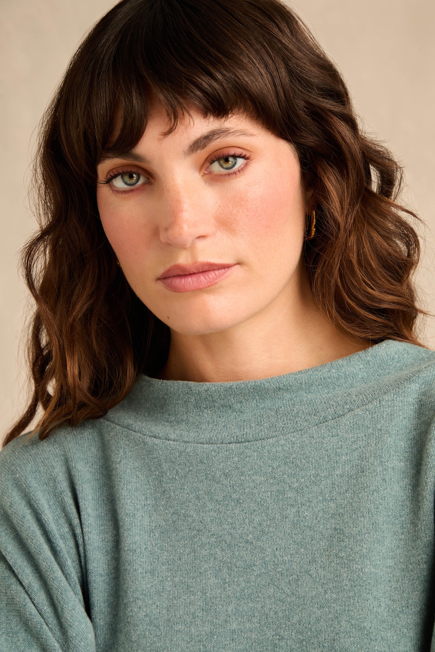 A woman with wavy brown hair and green eyes wears the Teal Soft Jersey Boxy Top and small hoop earrings, looking directly at the camera with a neutral expression.