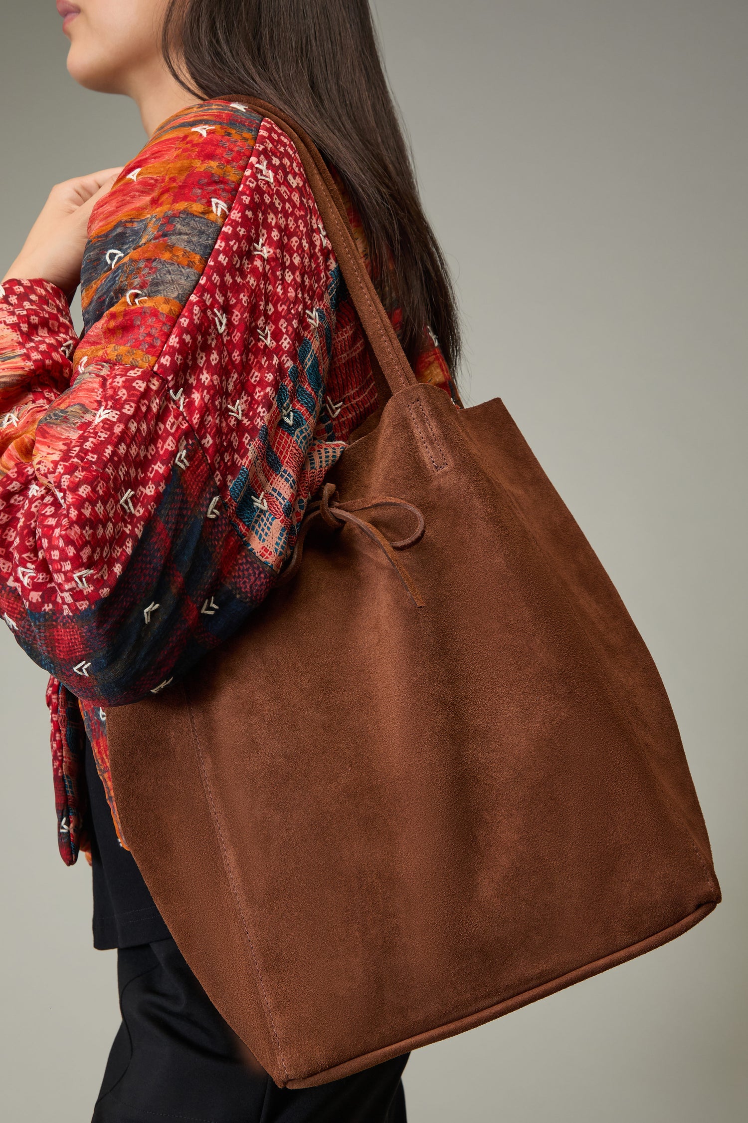 A person wearing a colorful patterned jacket carries the Soft Suede Tote Bag over their shoulder against a plain background.