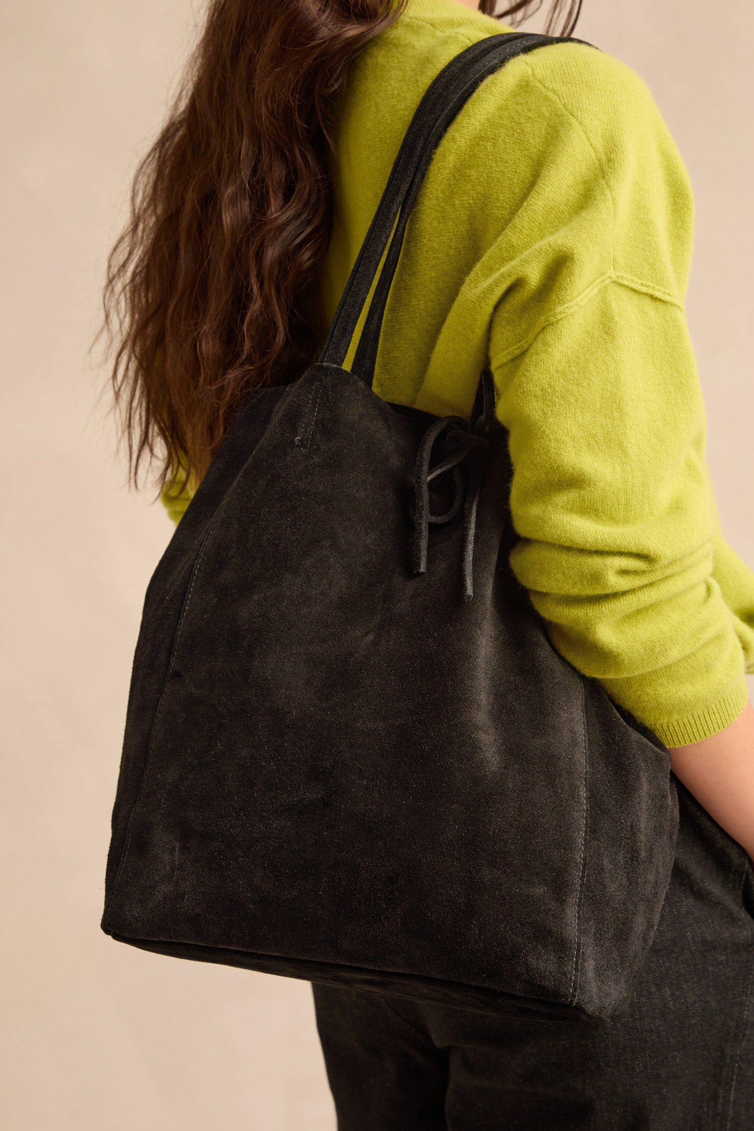 A person wearing a bright green sweater and black pants carries the Soft Suede Black Tote Bag over their shoulder.