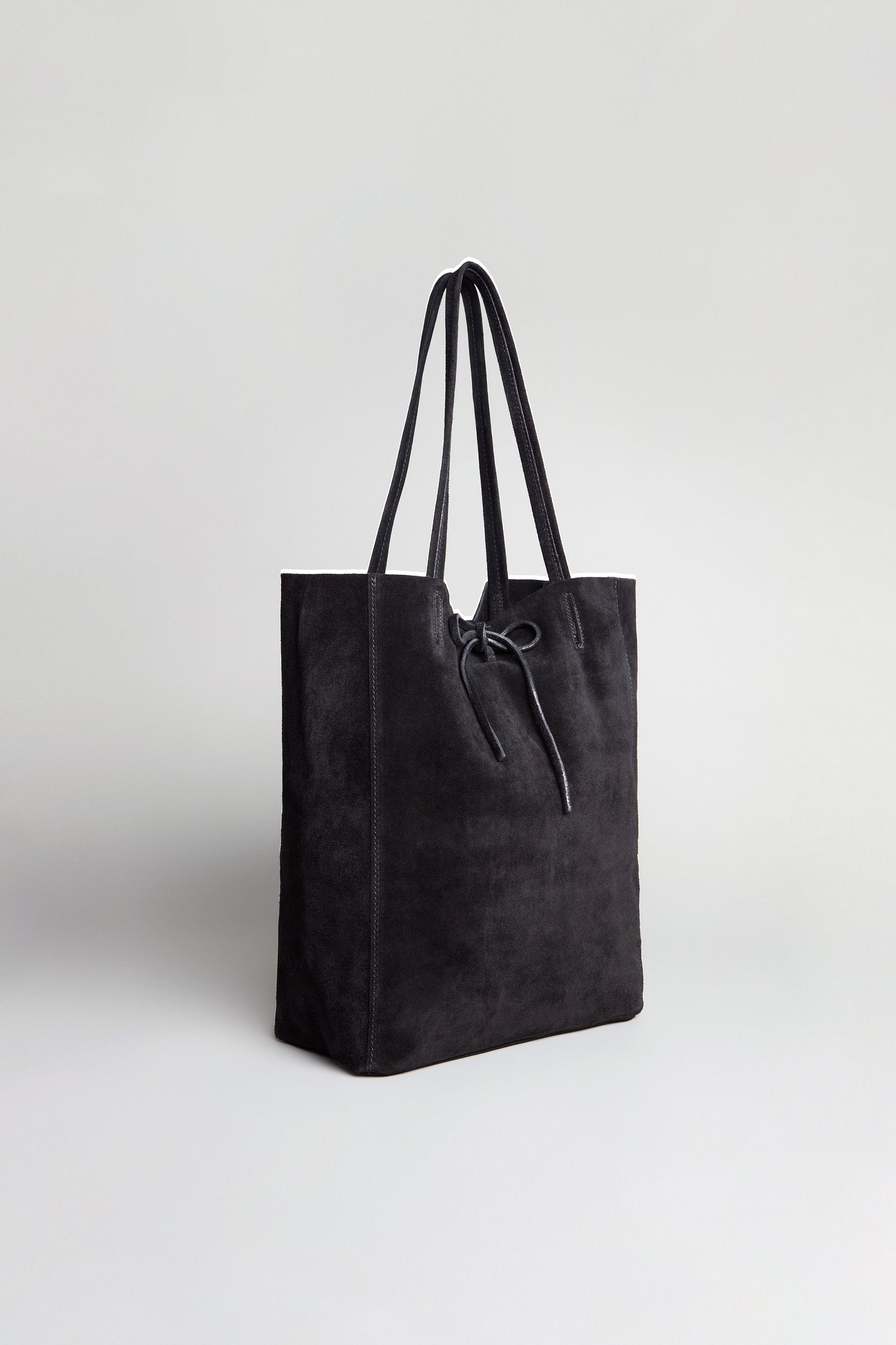 The Soft Suede Black Tote Bag, featuring two handles and a drawstring closure, is displayed upright against a plain light gray background.