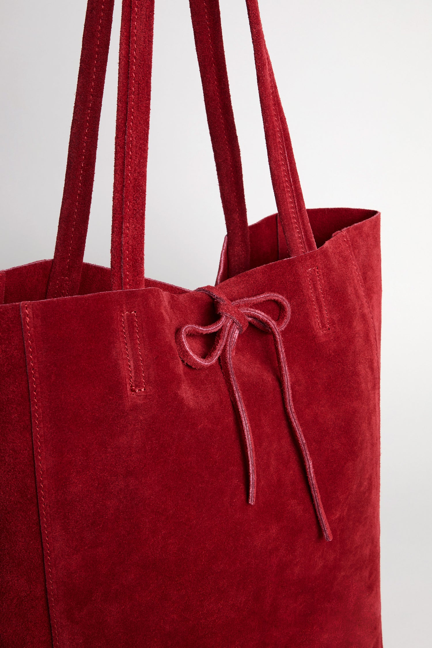 A close-up of the Soft Suede Poppy Tote Bag, showcasing its minimalist design with double handles and a tied suede drawstring near the opening, set against a plain background.