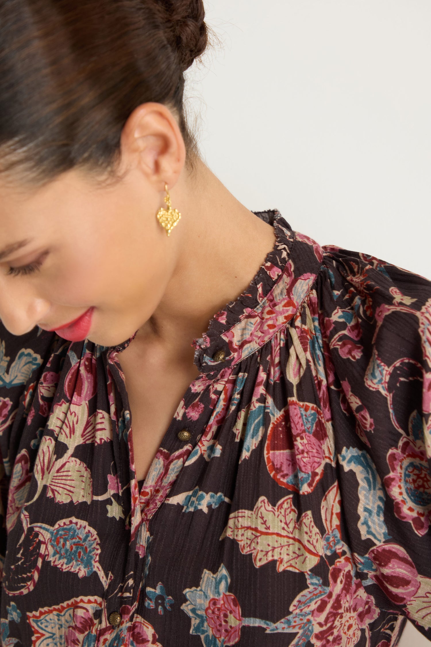 A woman with dark hair in an updo wears the Iris Print Tiered Dress and gold geometric earrings, looking down against a plain background.