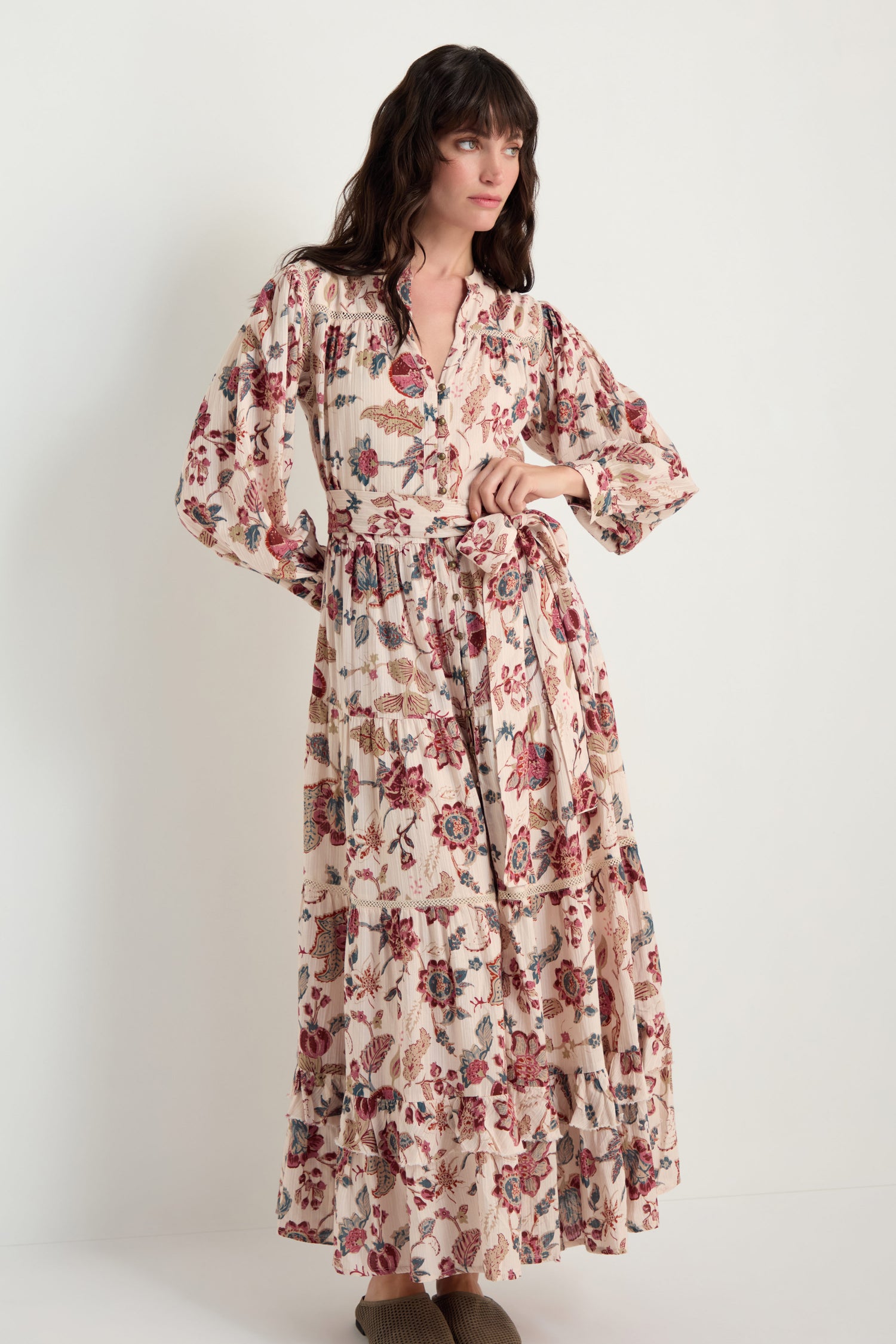 A woman wears the Floral Button-Through Tiered Dress, featuring long sleeves and a tied waist, standing against a plain white background.